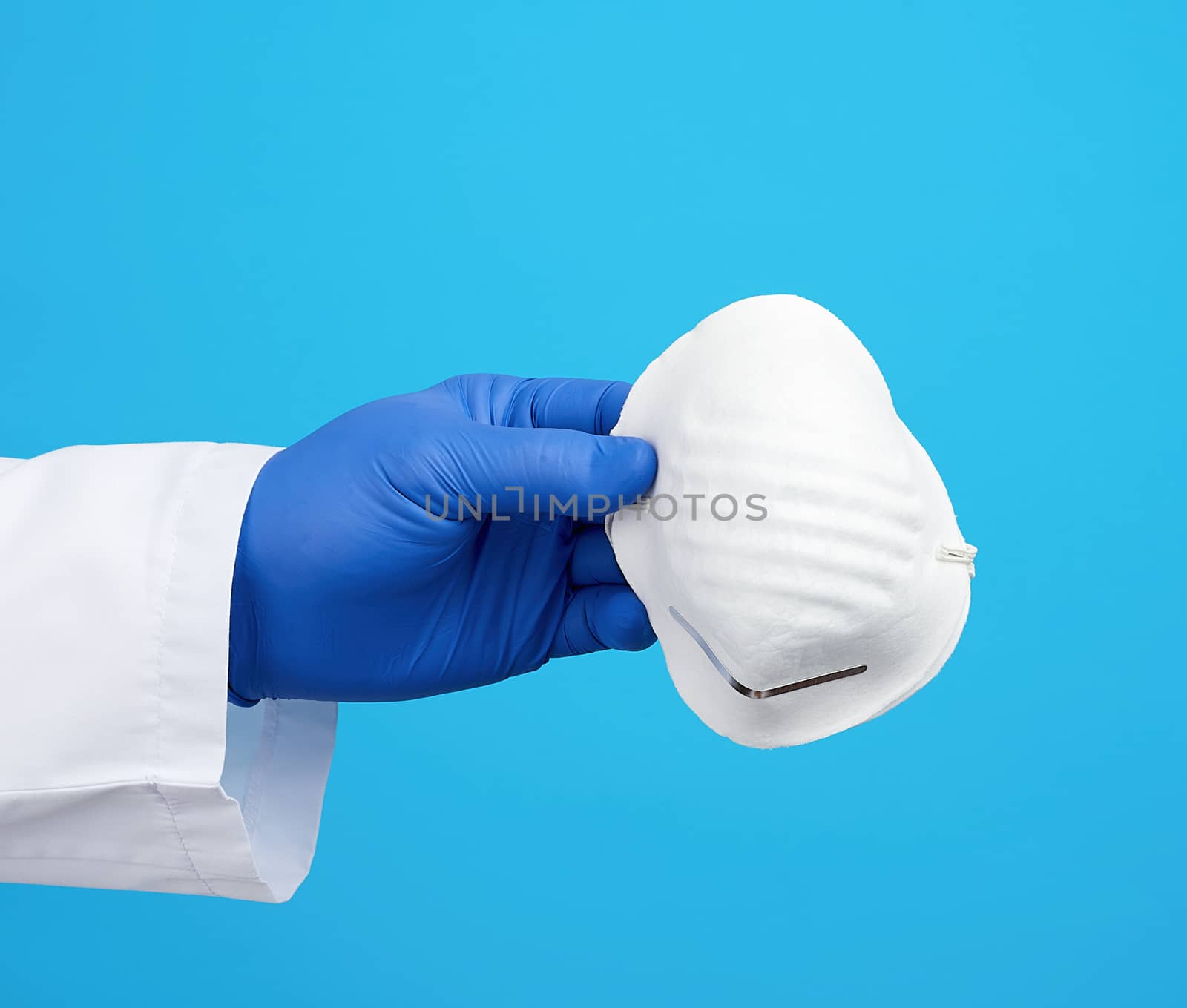 doctor in a white coat, blue latex sterile gloves holds textile disposable  masks in his hand on a blue background, additional protection against viruses during an epidemic, pandemic