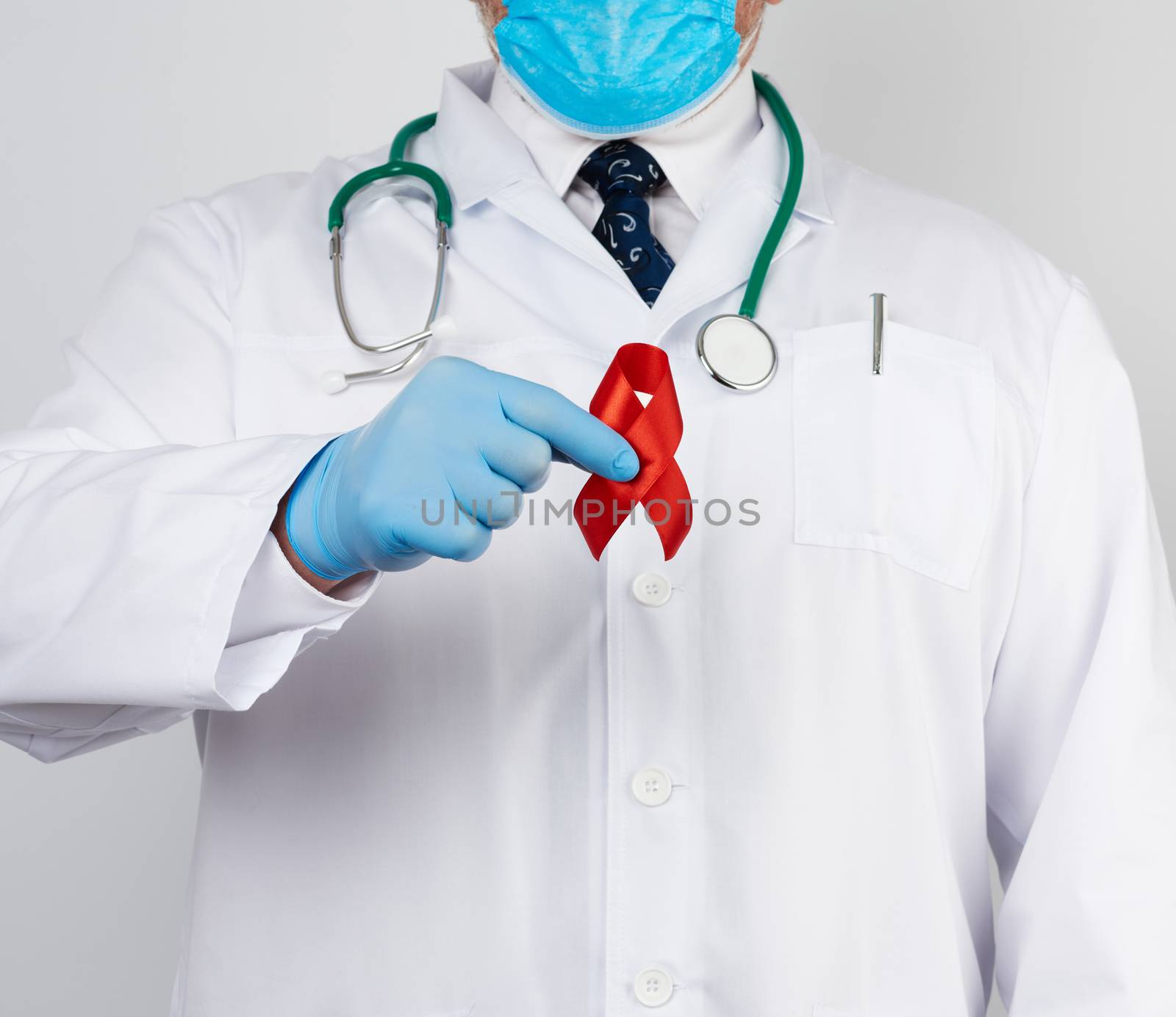 doctor in white uniform and sterile latex gloves holds a red ribbon-symbol of the fight against disease AIDS and vasculitis, close up