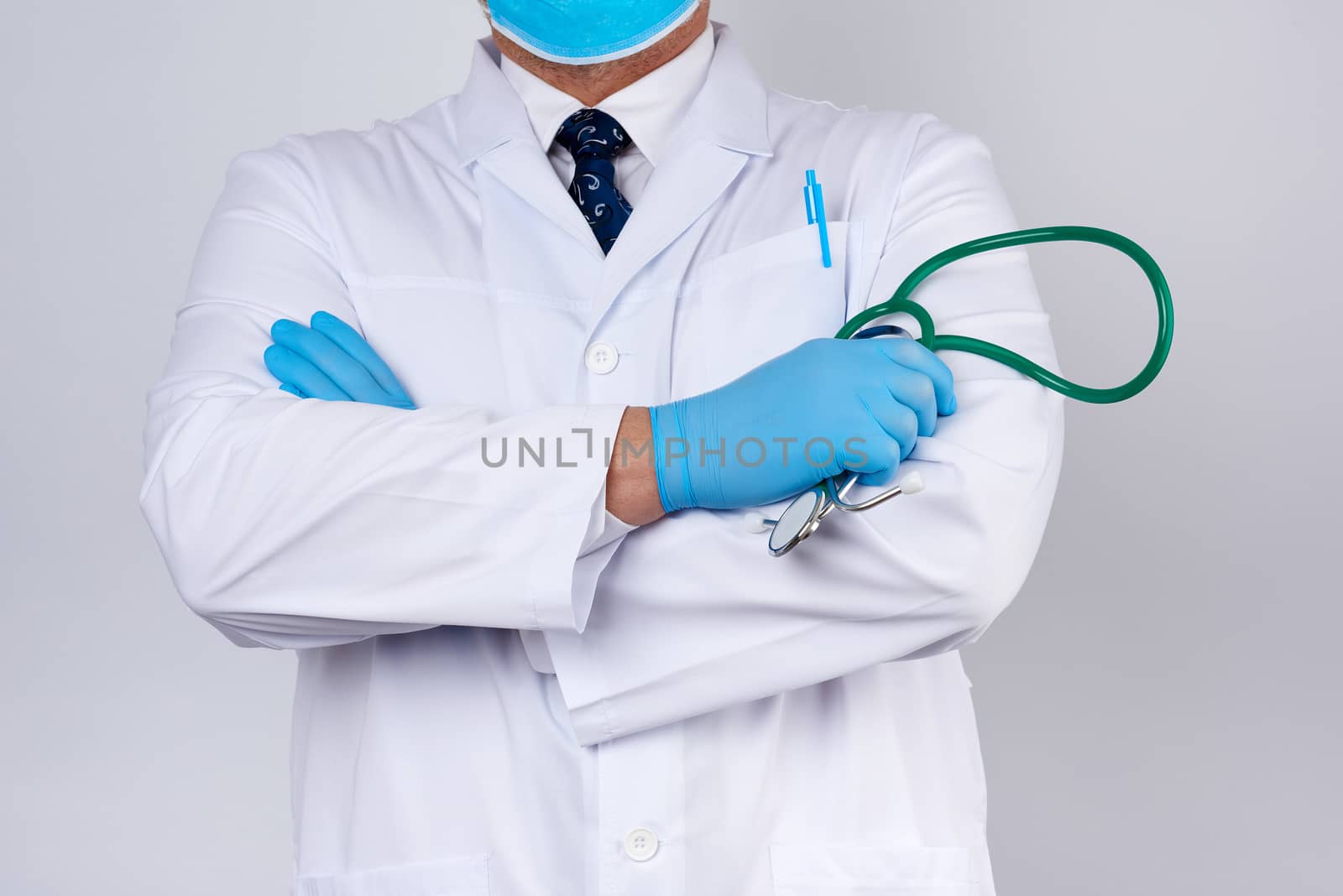 adult male doctor in a white medical coat stands and holds a green stethoscope on a white background