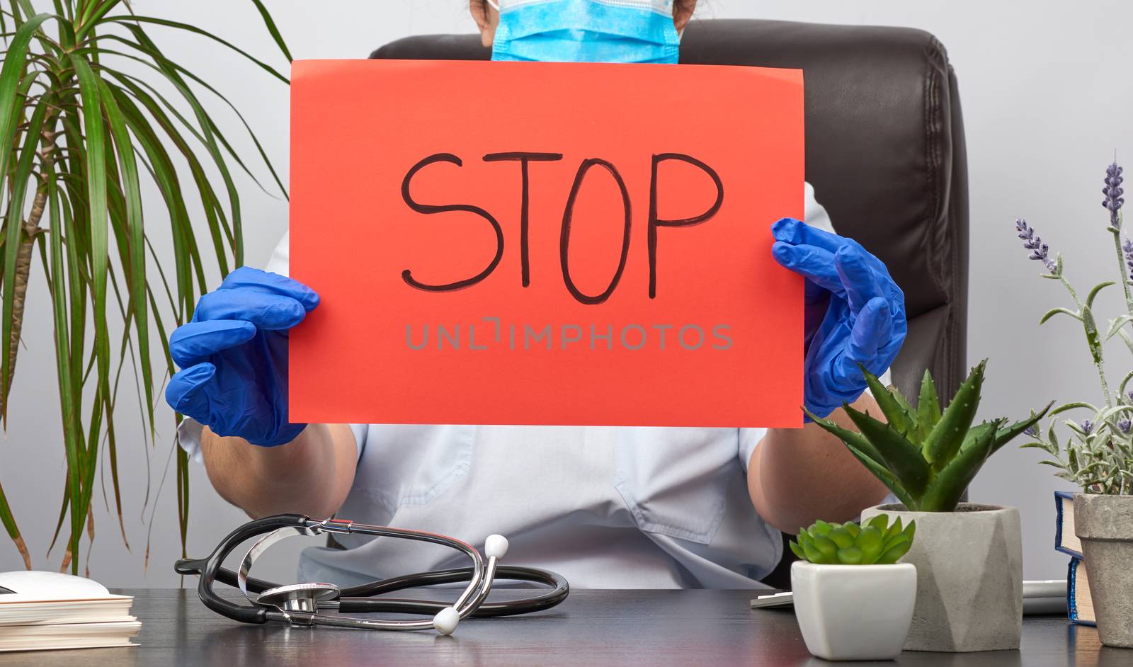 female medic is sitting in a brown leather chair in the office holding a red sheet of paper with the words stop, concept is not to panic, keep calm