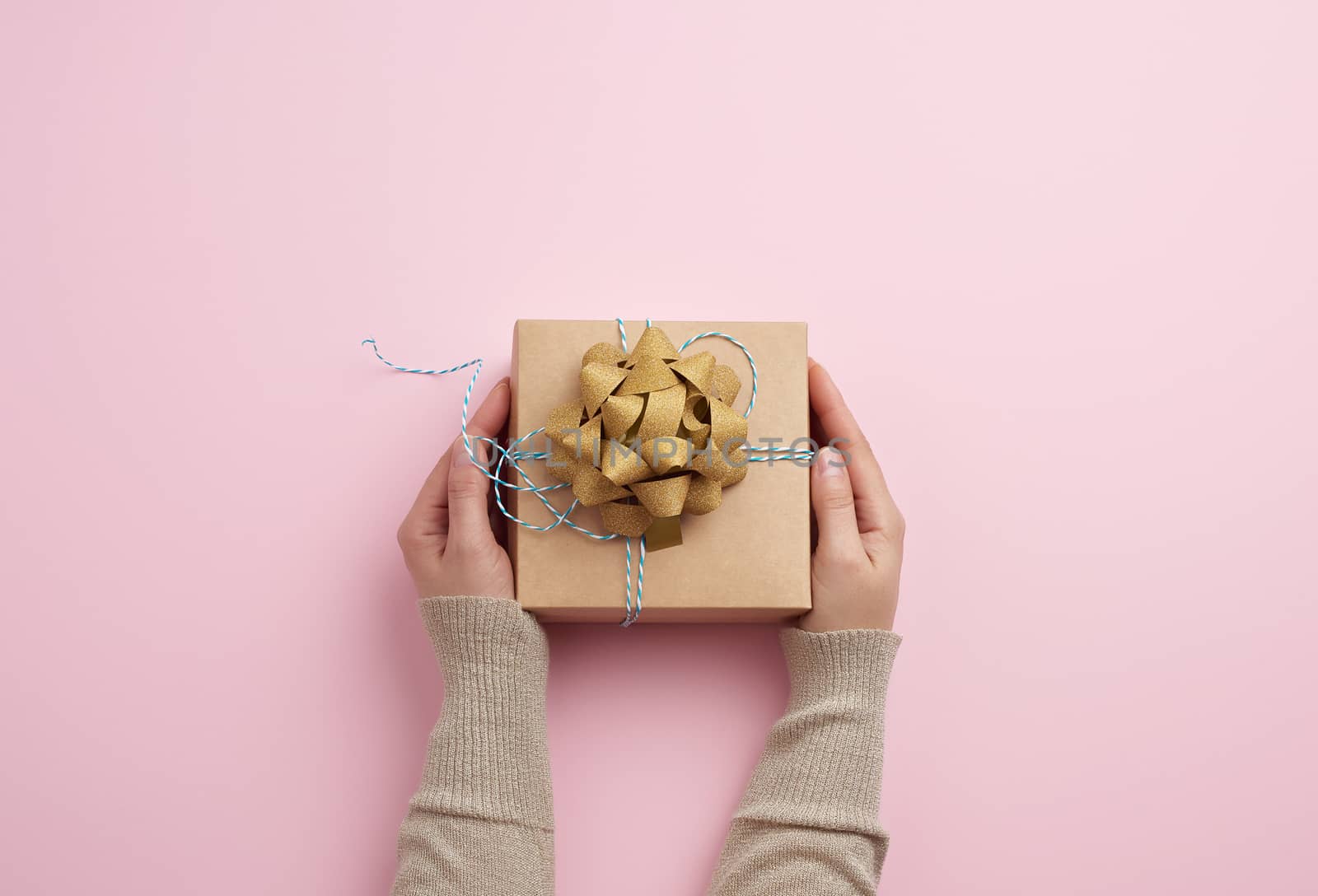 female hand holds a square box with a bow on a pink background, concept of a congratulation on a happy birthday
