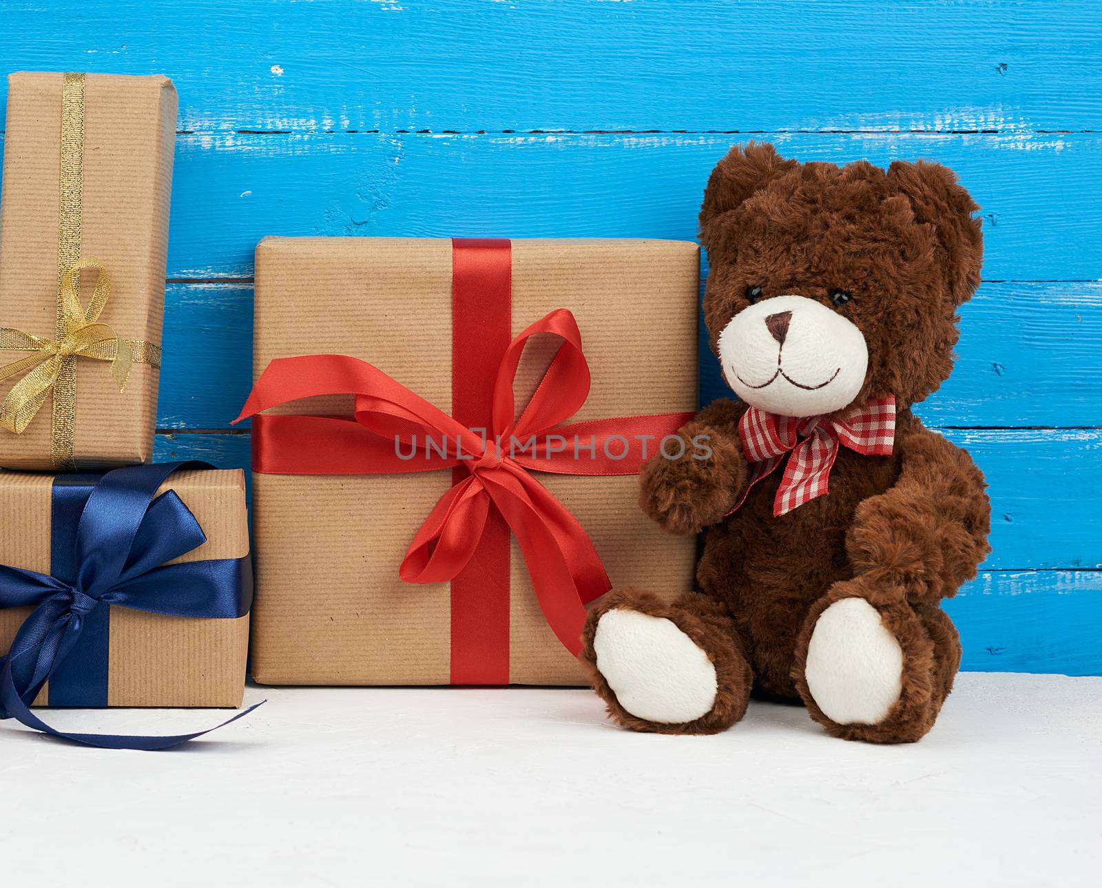 cute brown teddy bear sits on a blue wooden background, bouquet of red tulips and gift box, festive backdrop for birthday, Valentine's day, anniversary