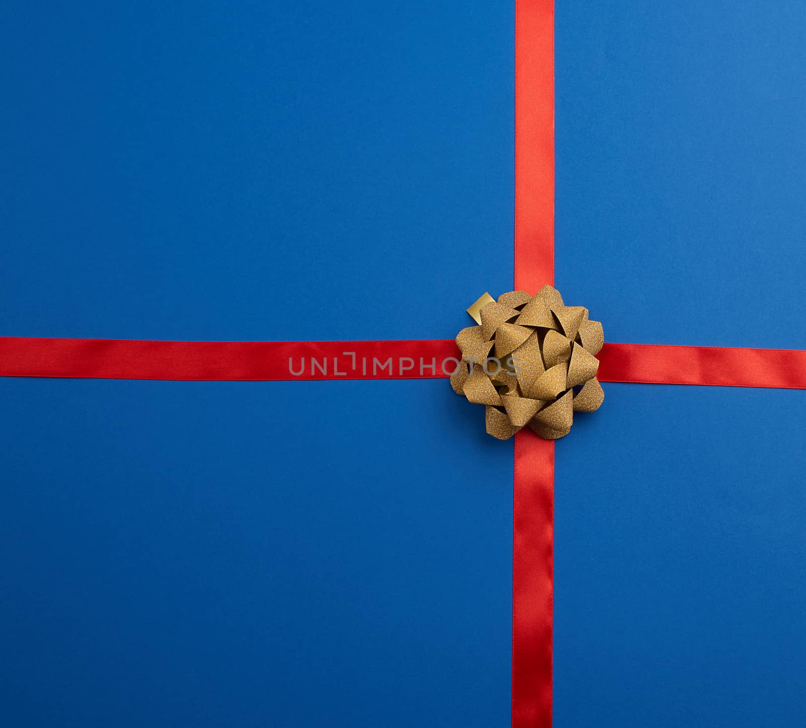 blue silk ribbon crossed on a dark blue background in the middle of a golden bow, imitation of tying a gift, top view