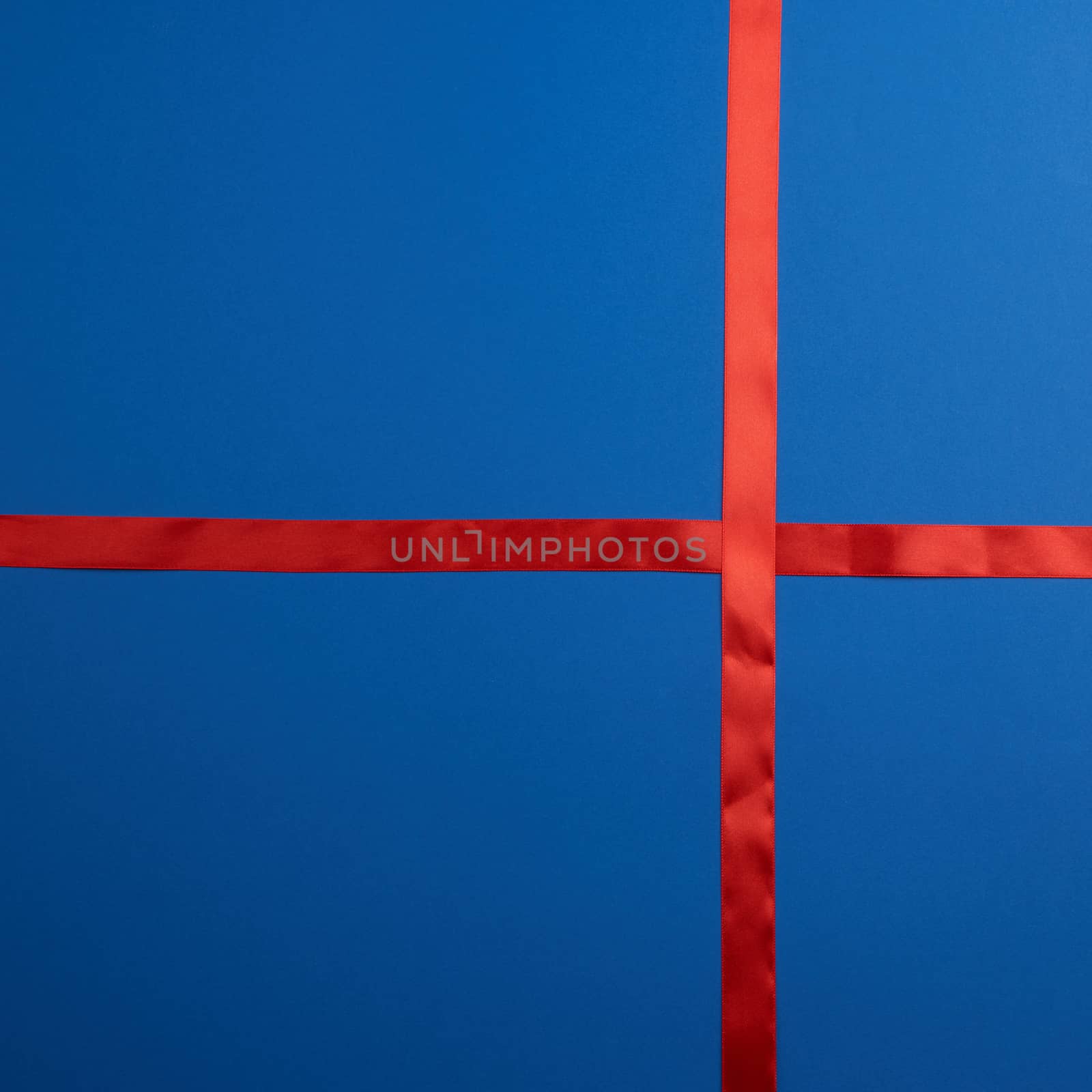 red silk ribbon crossed on a dark blue background, imitation of tying a gift, top view