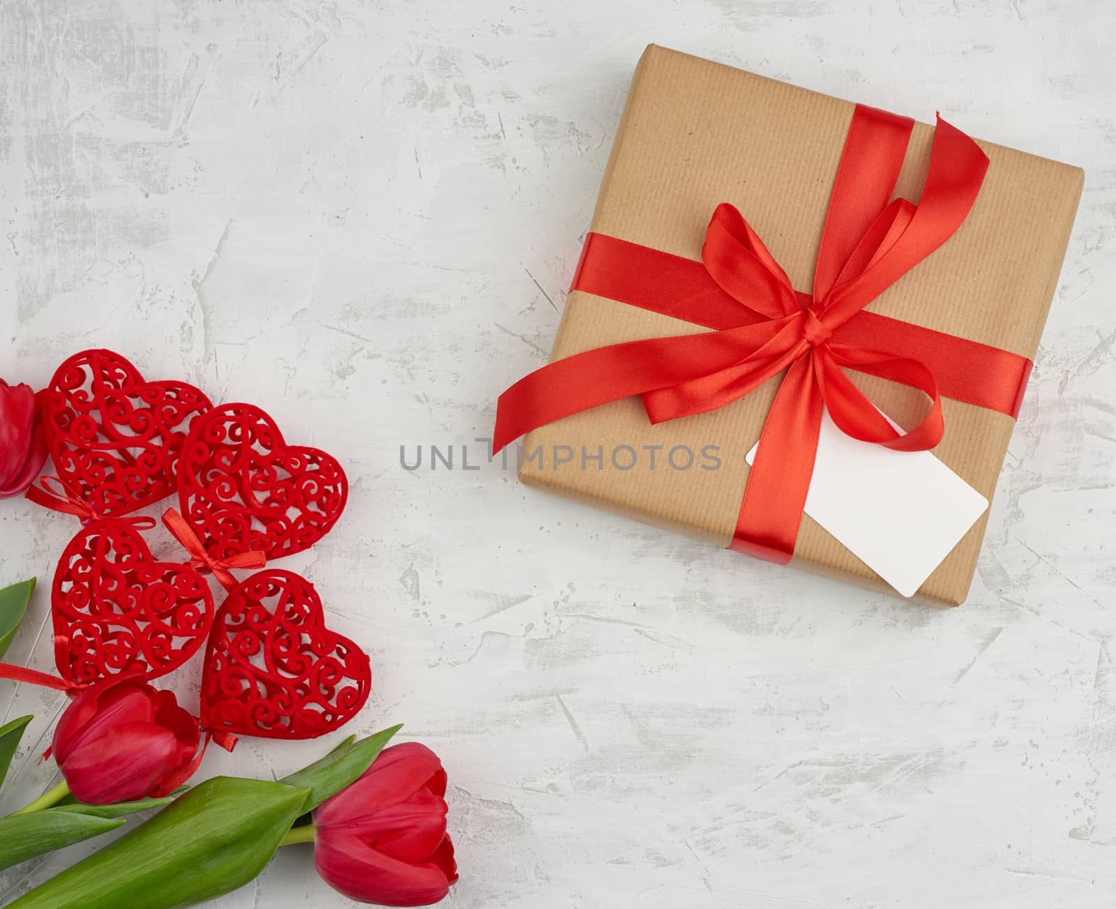 bouquet of red blooming tulips with green leaves, wrapped gift in brown craft paper on a white background. Festive backdrop for birthday, Valentine's day