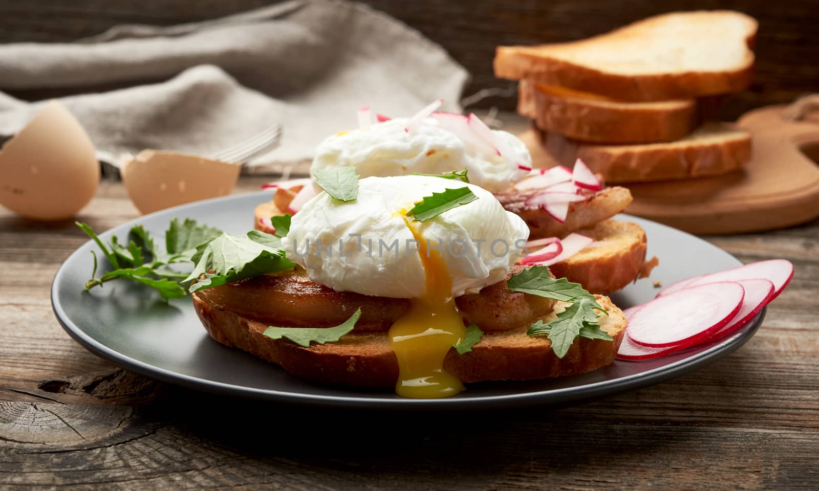  sandwiches on a toasted white slice of bread with poached eggs, green leaves of arugula and radish in a round plate, morning breakfast