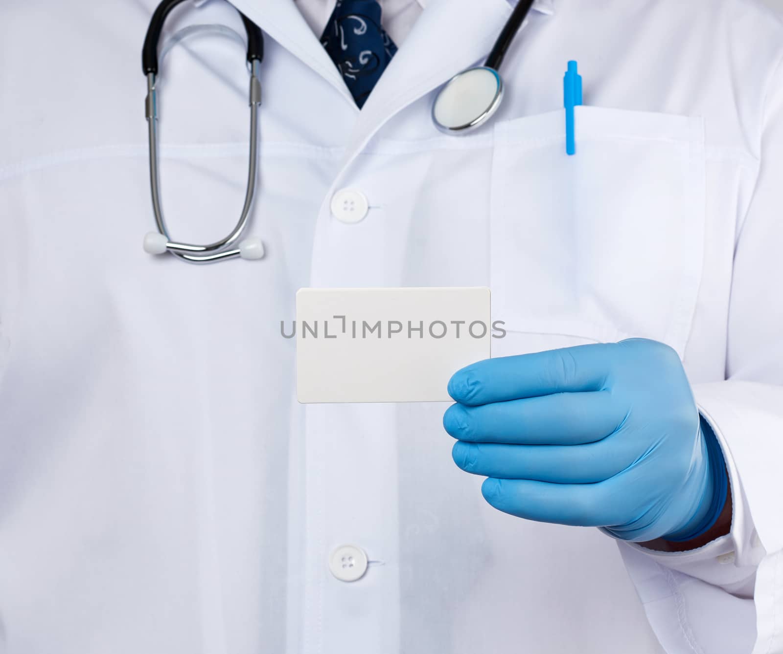 doctor therapist is dressed in a white robe uniform and blue sterile gloves is standing and holding a stack of empty white paper business cards, place for inscription