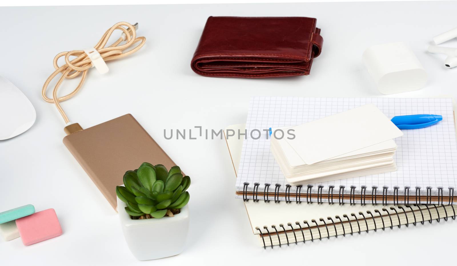 notebooks, pen, stack of business cards, brown leather wallet and power bank with a cord on a white table, workplace