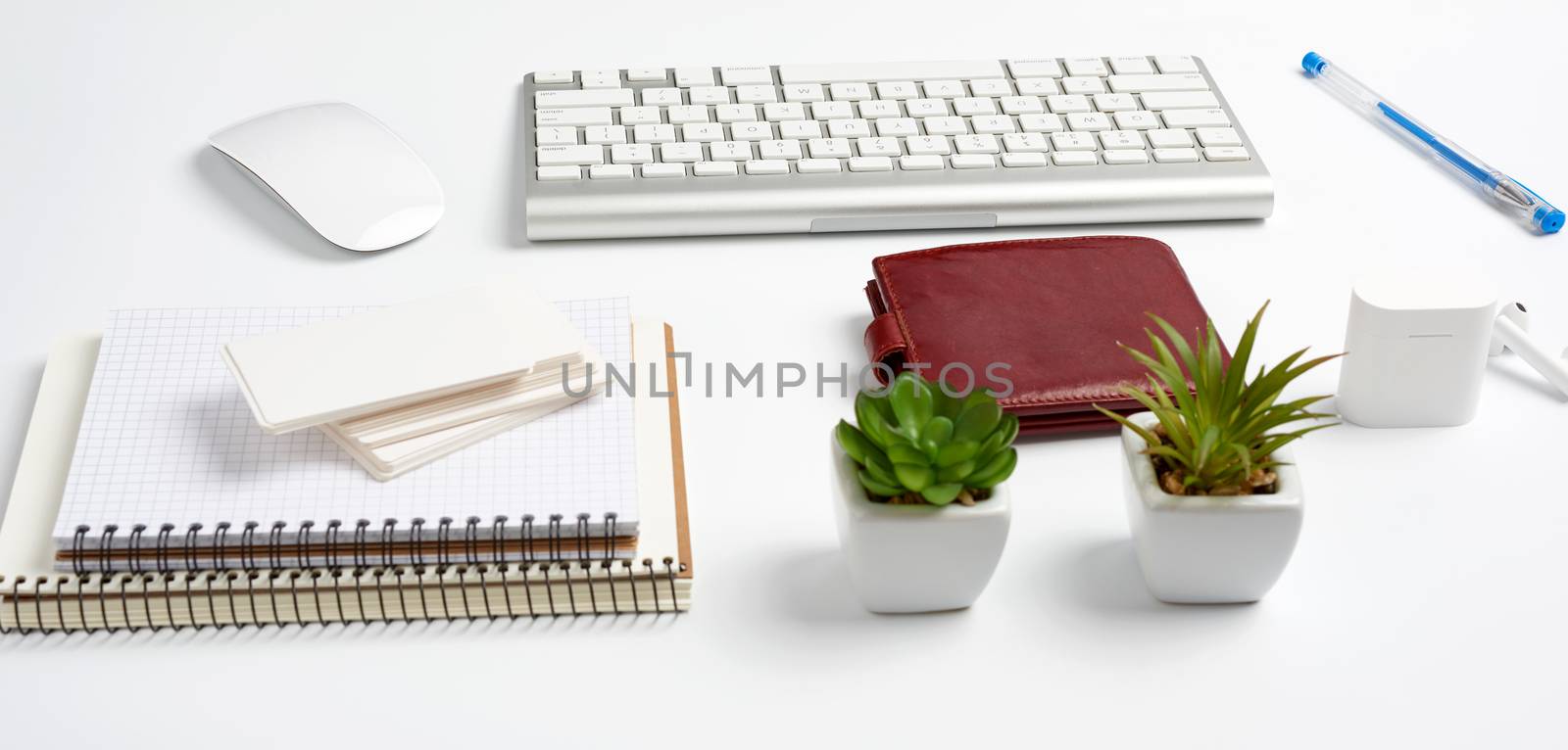 White wireless keyboard, a stack of notebooks, green plants in pots and a mouse, workplace of a freelancer, businessman. White table