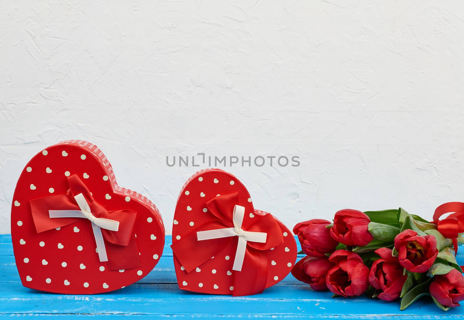 bouquet of red blooming tulips with green leaves, wrapped gifts on a blue wooden background. Festive backdrop for birthday, Valentine's day, anniversary