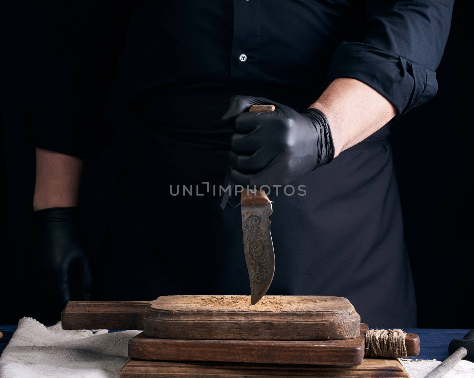 chef in a black shirt and black latex gloves holds a vintage kitchen knife for cutting meat, low key