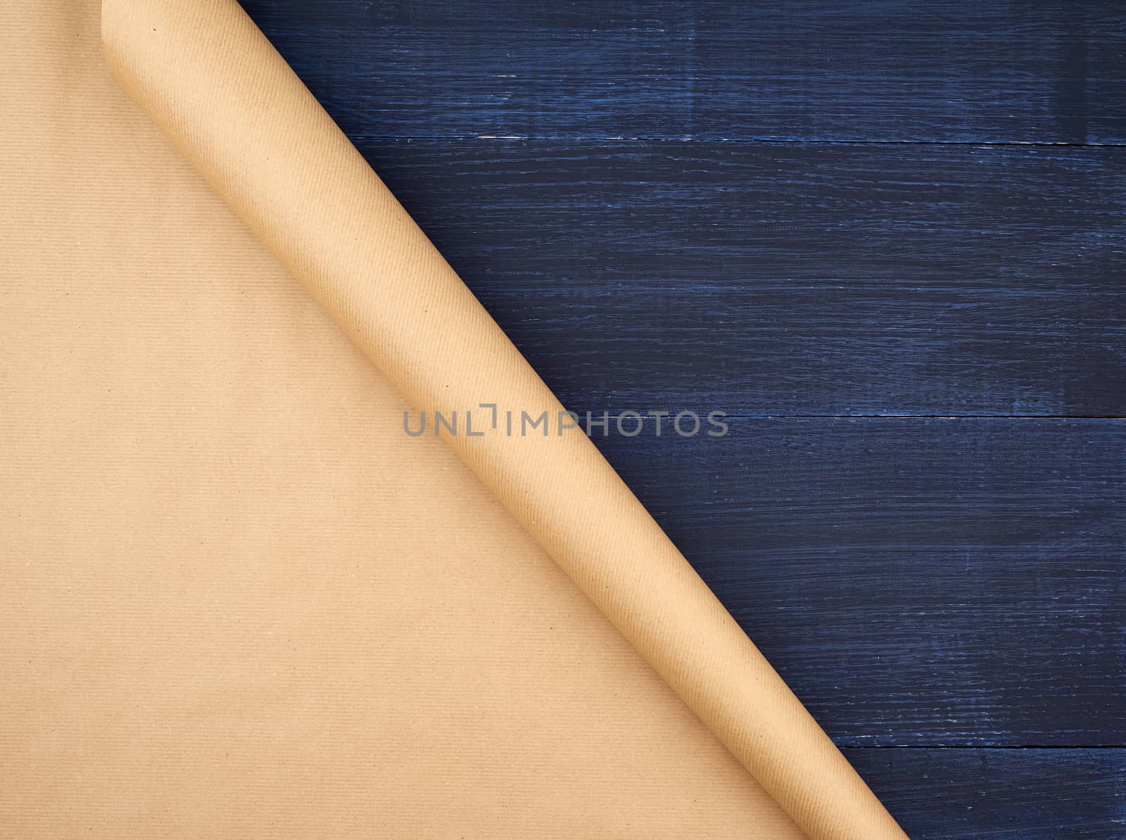 untwisted roll of brown craft paper on a blue wooden background, empty space. Old craft paper texture. Clean sheet, template, angle is twisted