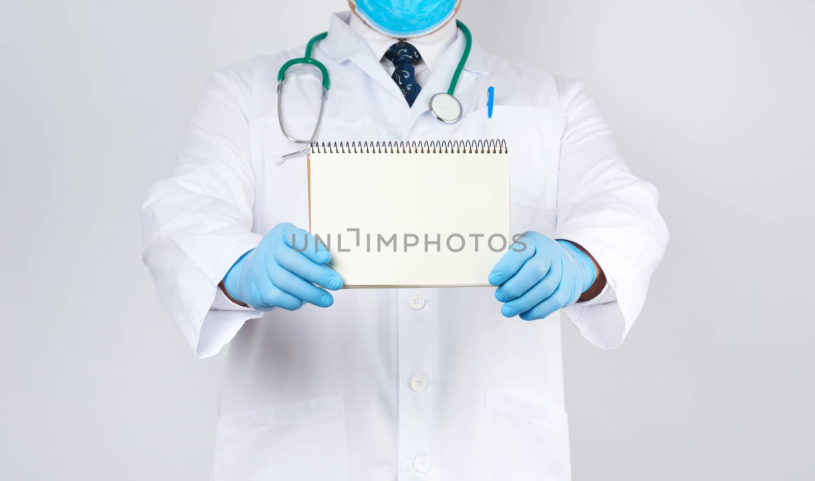 male doctor in a white coat and medical blue gloves holds a notebook with blank white sheets on a white background, place for an inscription