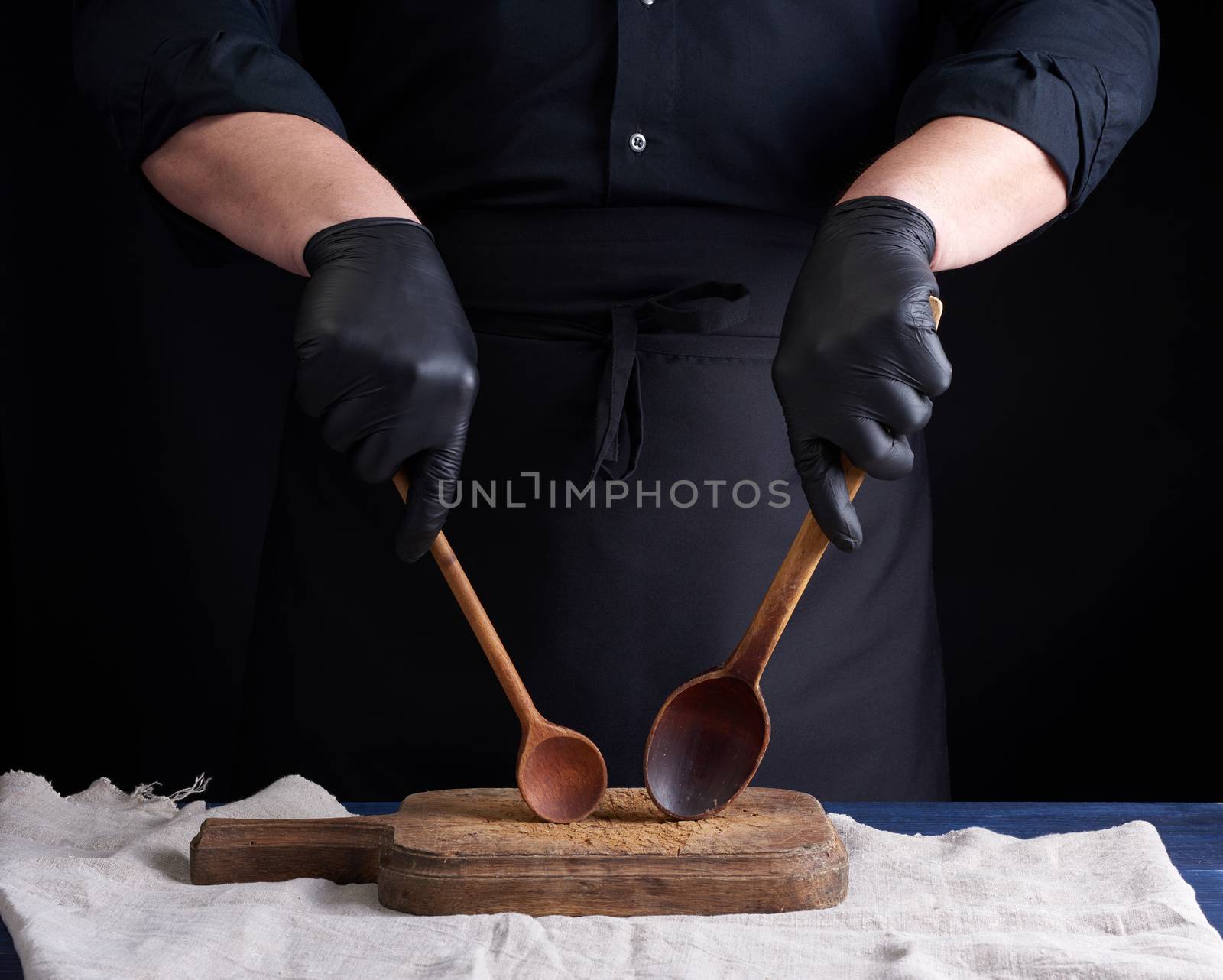 chef in black latex gloves and a black uniform holds wooden vintage spoons in front of him, low key