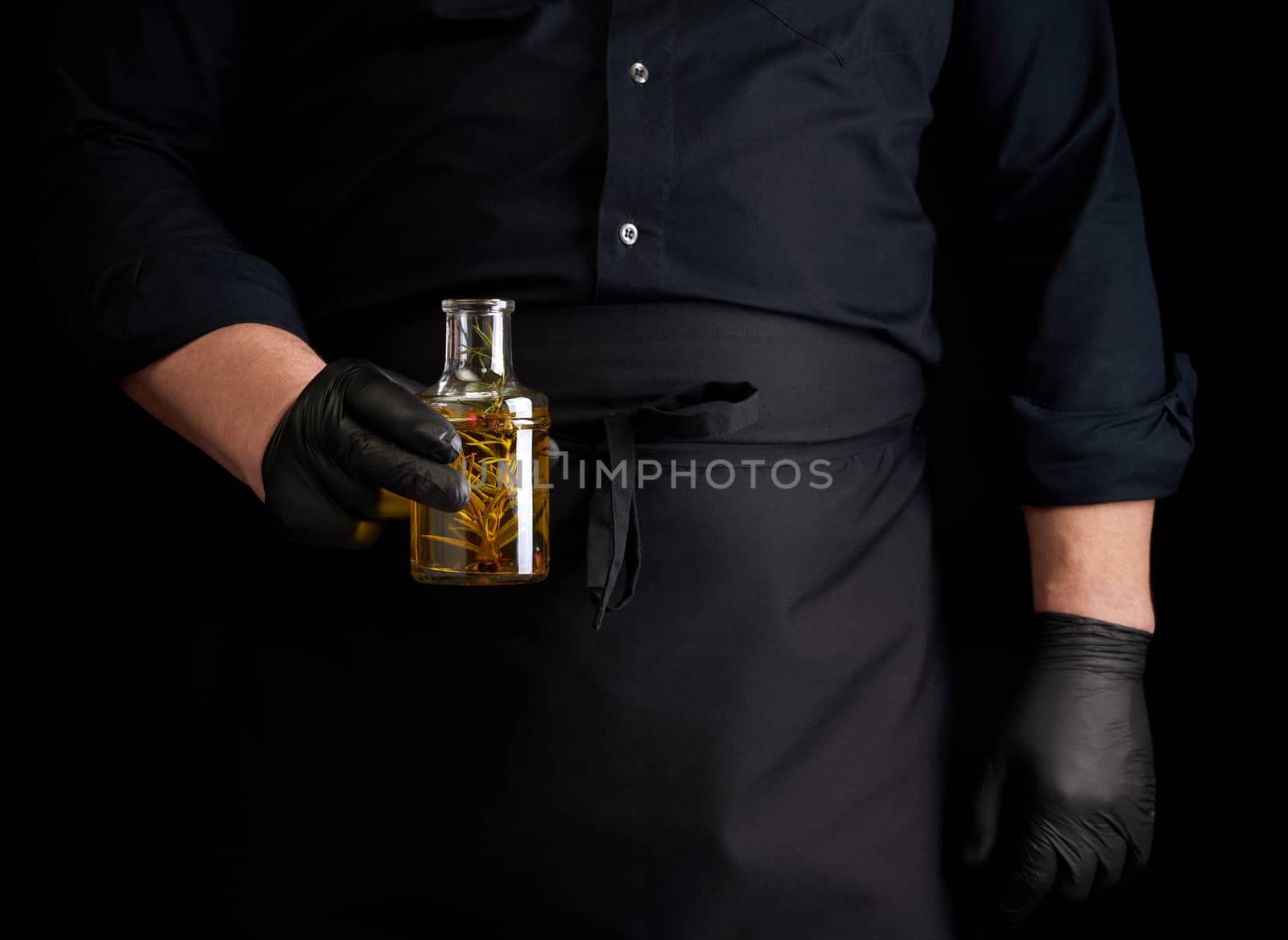 man in black clothes, latex gloves holds a transparent bottle with olive oil, low key