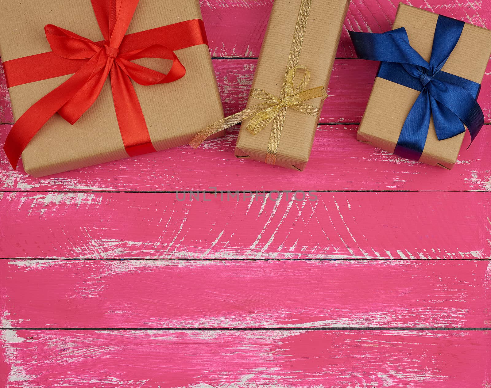 gifts wrapped in brown kraft paper and a silk ribbon, pink wooden background. festive backdrop for birthday and valentines day