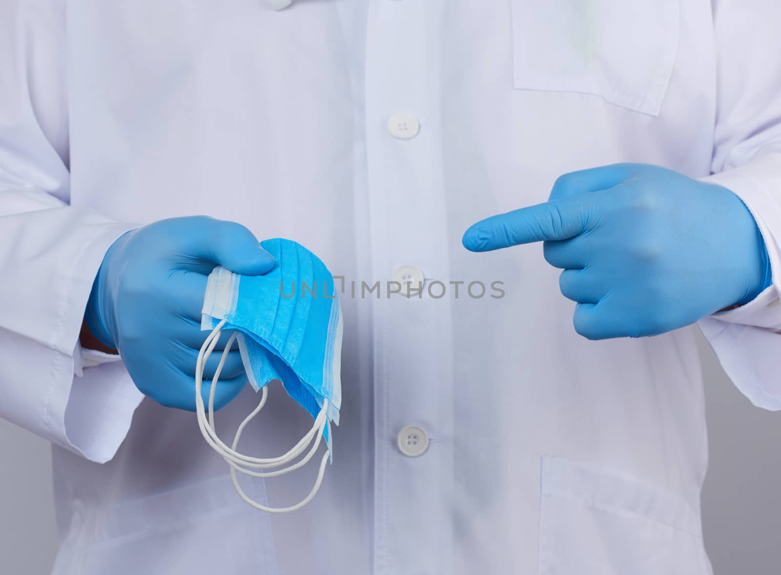 doctor in a white coat, blue latex sterile gloves holds textile medical masks in his hand, protective accessory against viruses and bacteria, close up