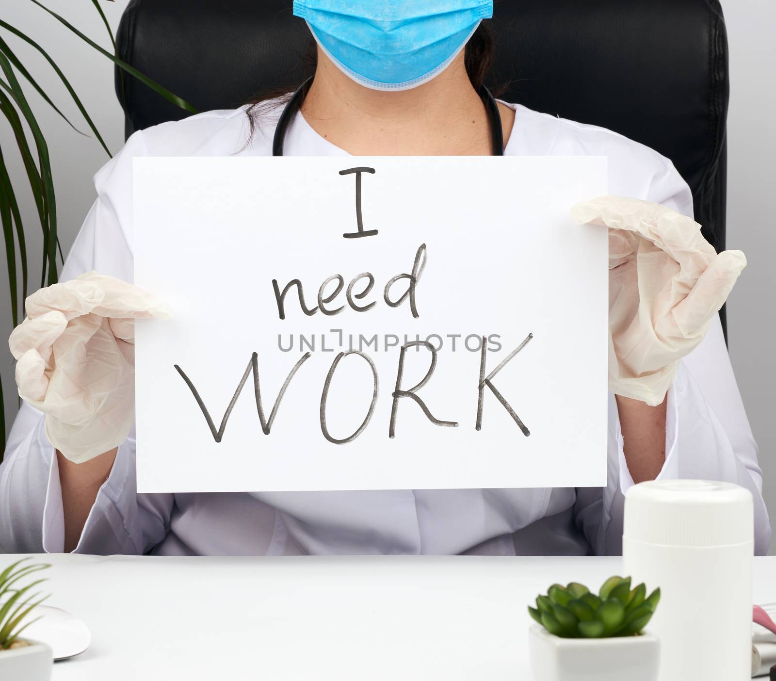 woman doctor in a white coat, sterile medical gloves holds a poster with the inscription I need work, concept of unemployment and job search