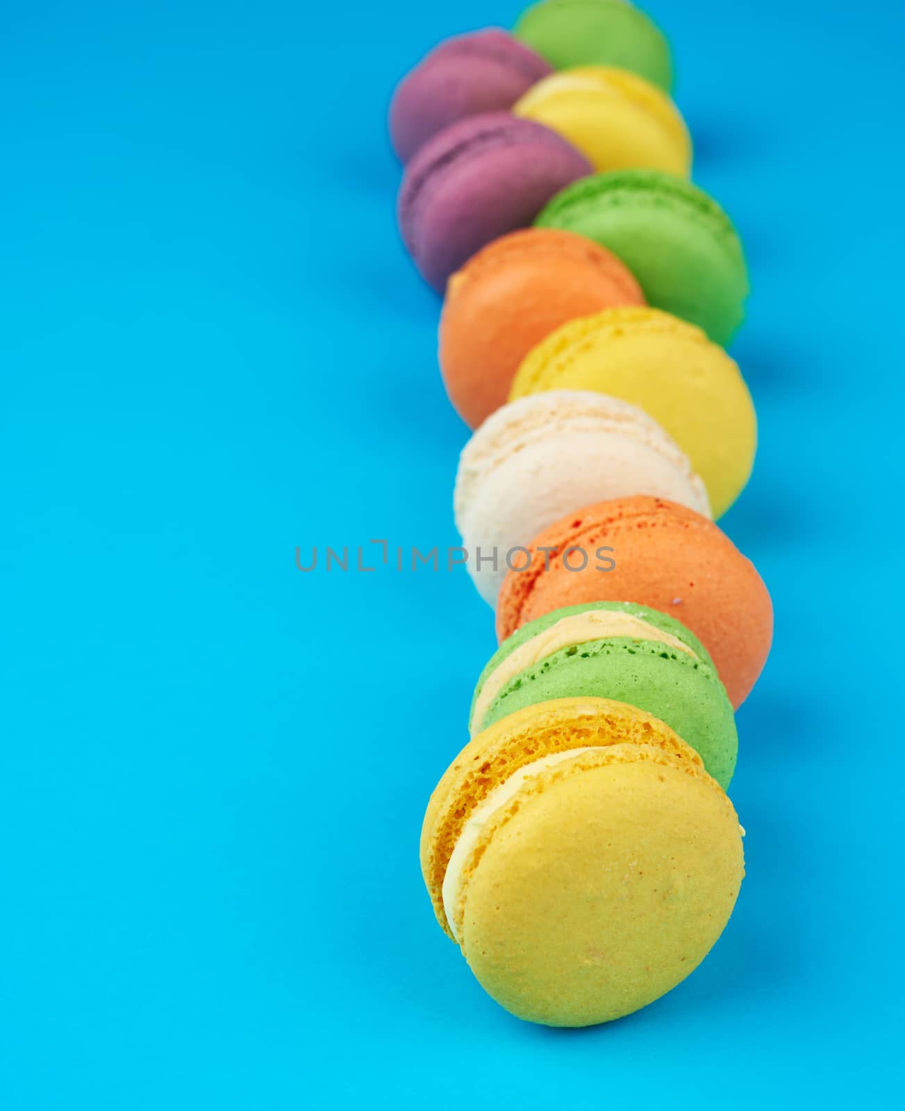 round multi-colored baked macarons with cream lie in a line on a blue background, close up