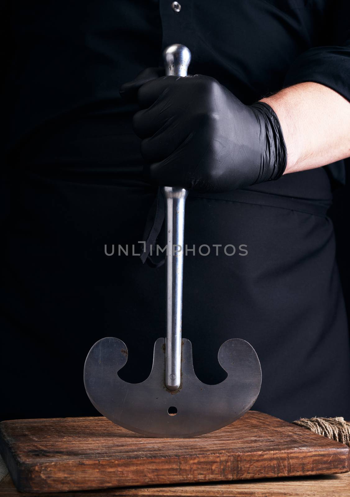 man in black clothes, latex gloves holds a vintage metal ax-knife for meat and vegetables, dark background