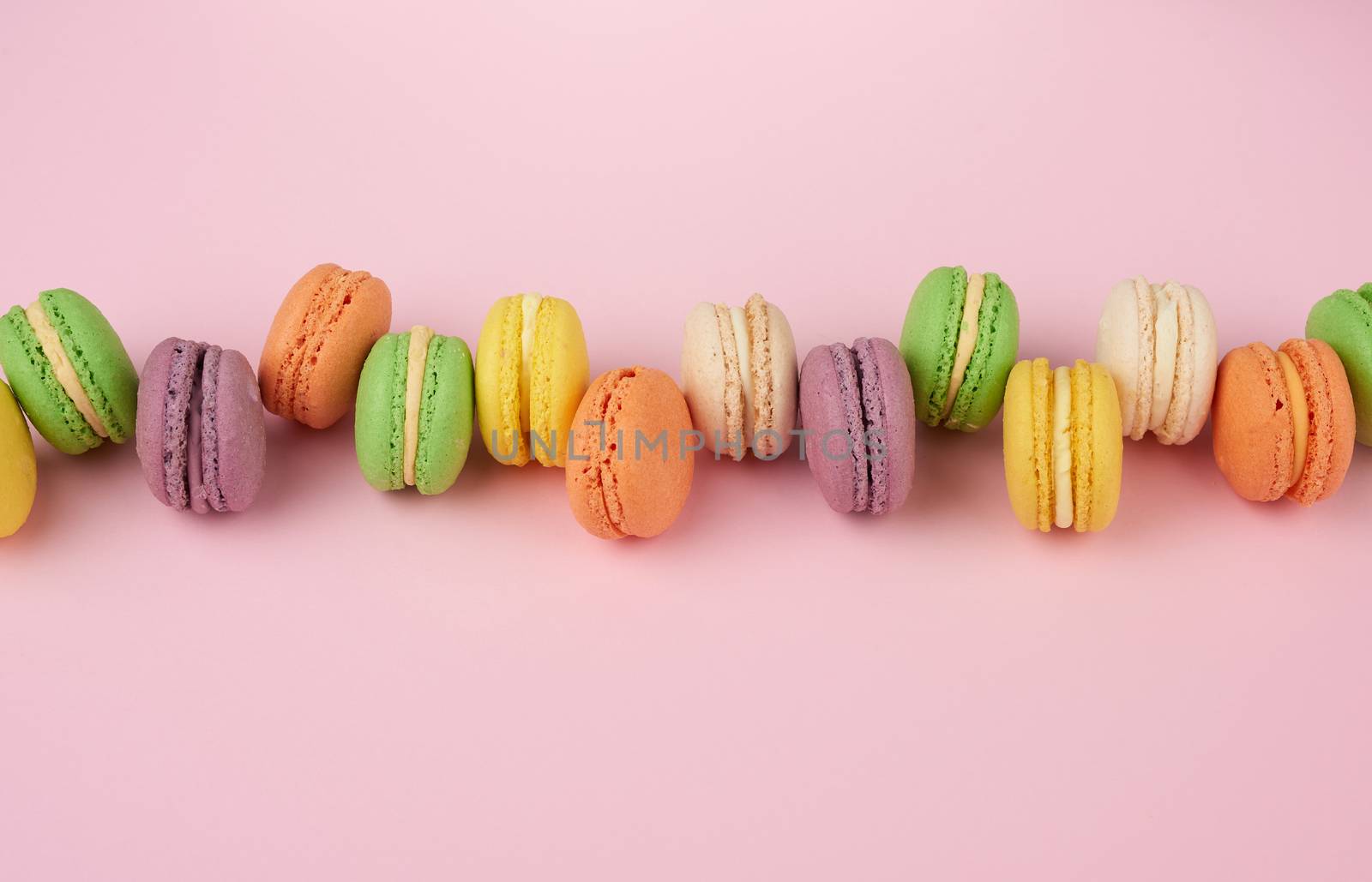many multi-colored round baked macarons cakes on a light pink background, top view