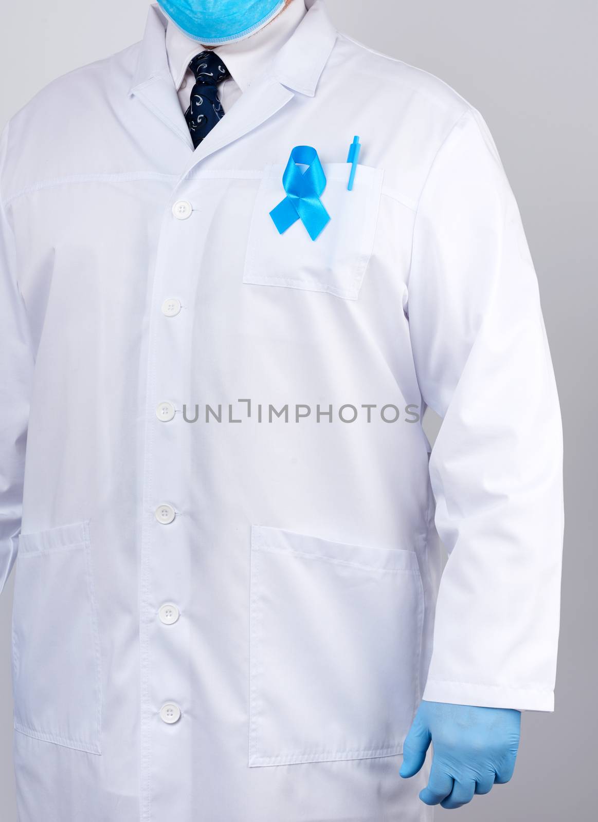 male doctor in a white coat and tie stands and holds a blue silk ribbon in a loop, wearing blue sterile medical gloves, symbol of the fight and treatment of prostate cancer