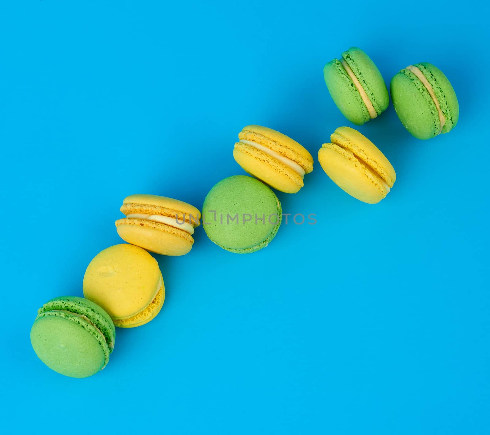 stack of yellow and green round almond flour cakes macarons with cream on a blue background, delicious pastry, top view