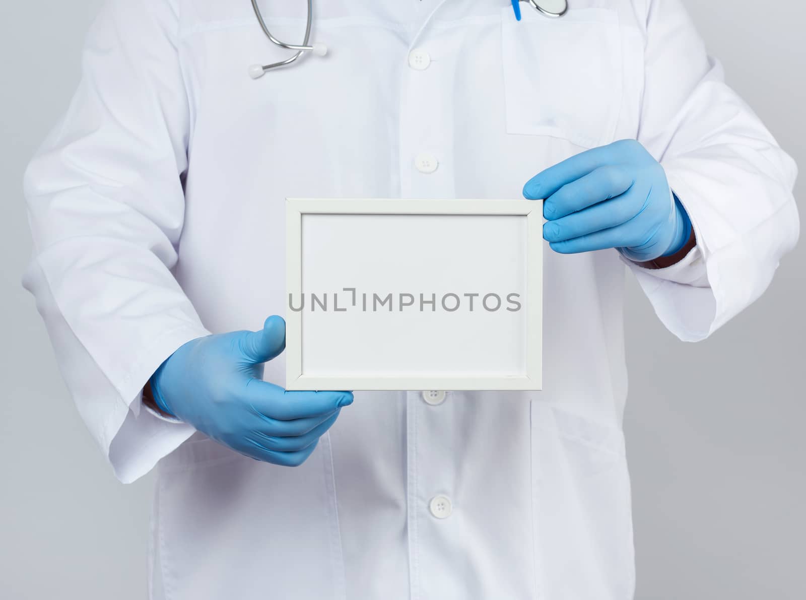 male doctor in a white medical coat and blue latex gloves holds an empty white frame for an inscription, template for a designer