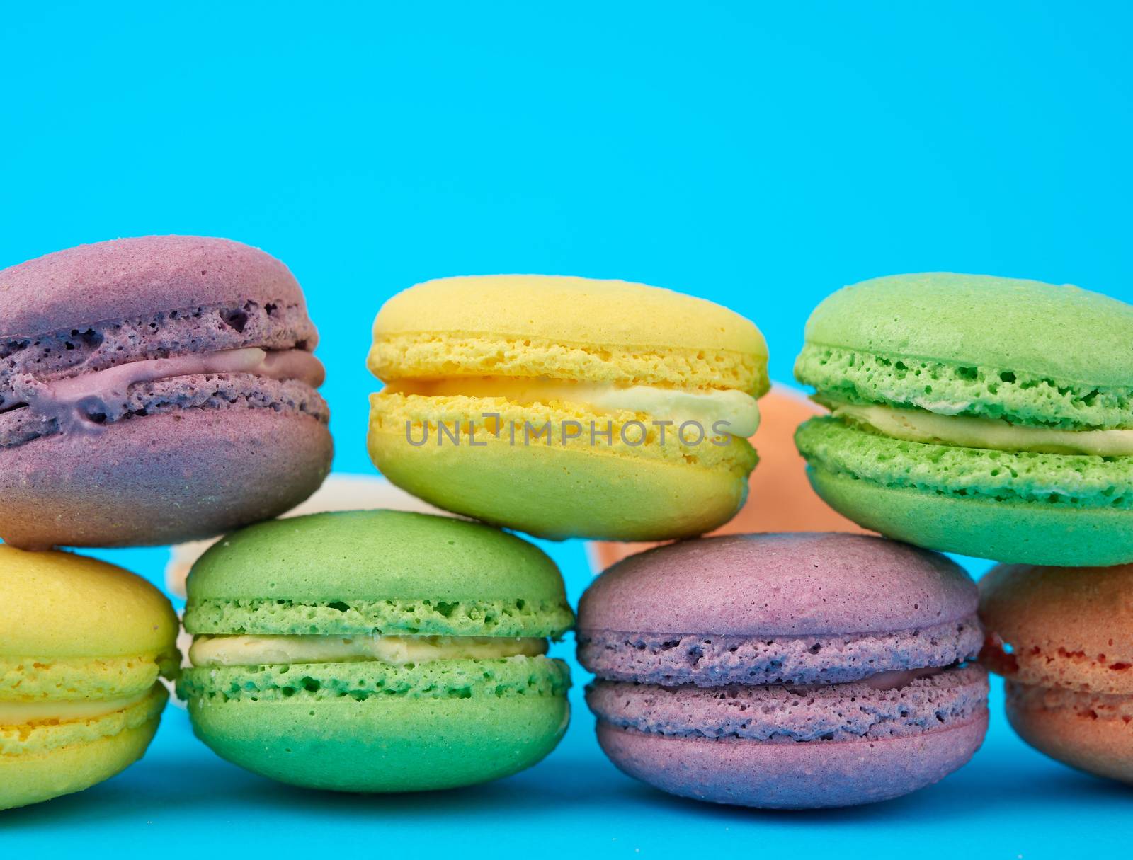 multi-colored round baked macarons cakes on a light blue background, close up