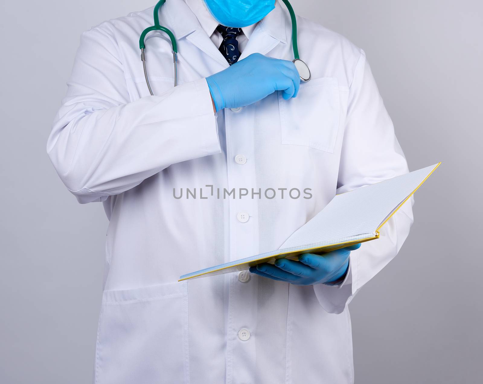 doctor in a white coat with buttons, wearing blue sterile gloves, holding a paper open notebook in his hand on a white studio background