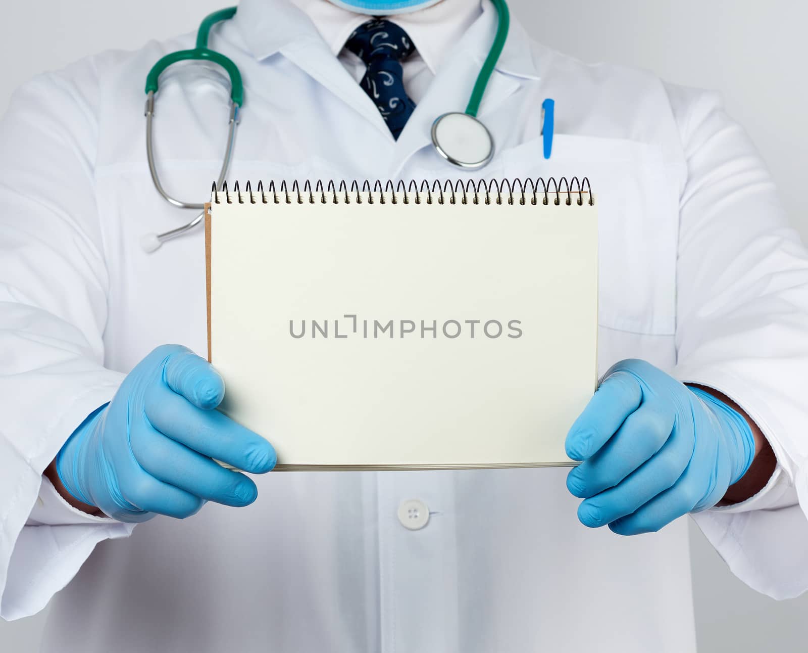 male doctor in a white coat and medical blue gloves holds a notebook with blank white sheets, place for an inscription