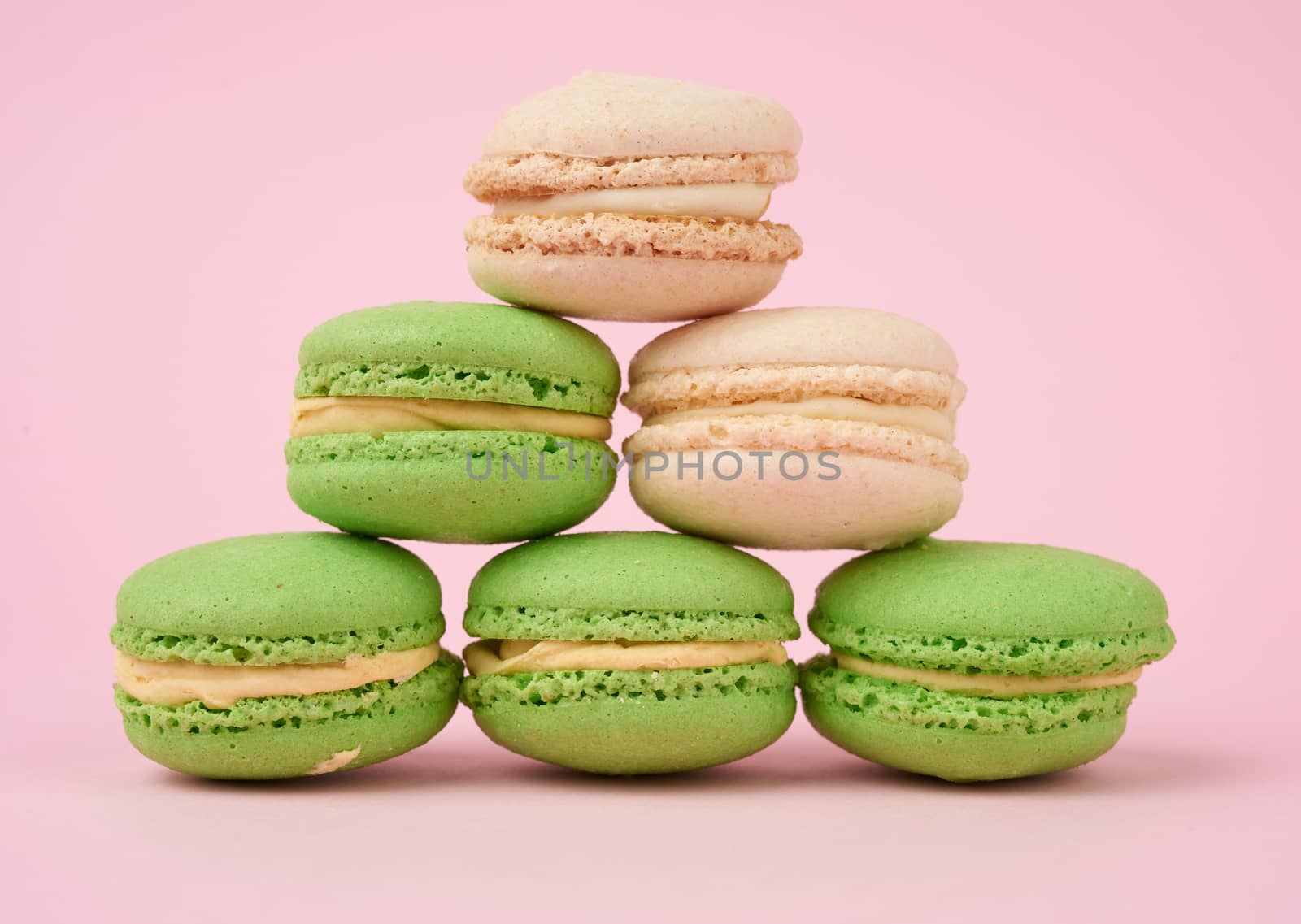 stack of white and green round almond flour cakes macarons with cream on a pink background, delicious cake