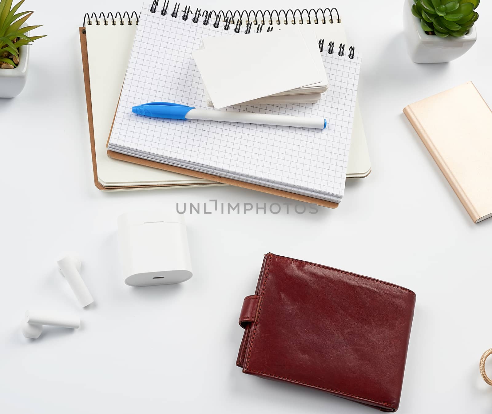 notebooks, pen, stack of business cards, brown leather wallet and power bank with a cord on a white table, workplace, top view
