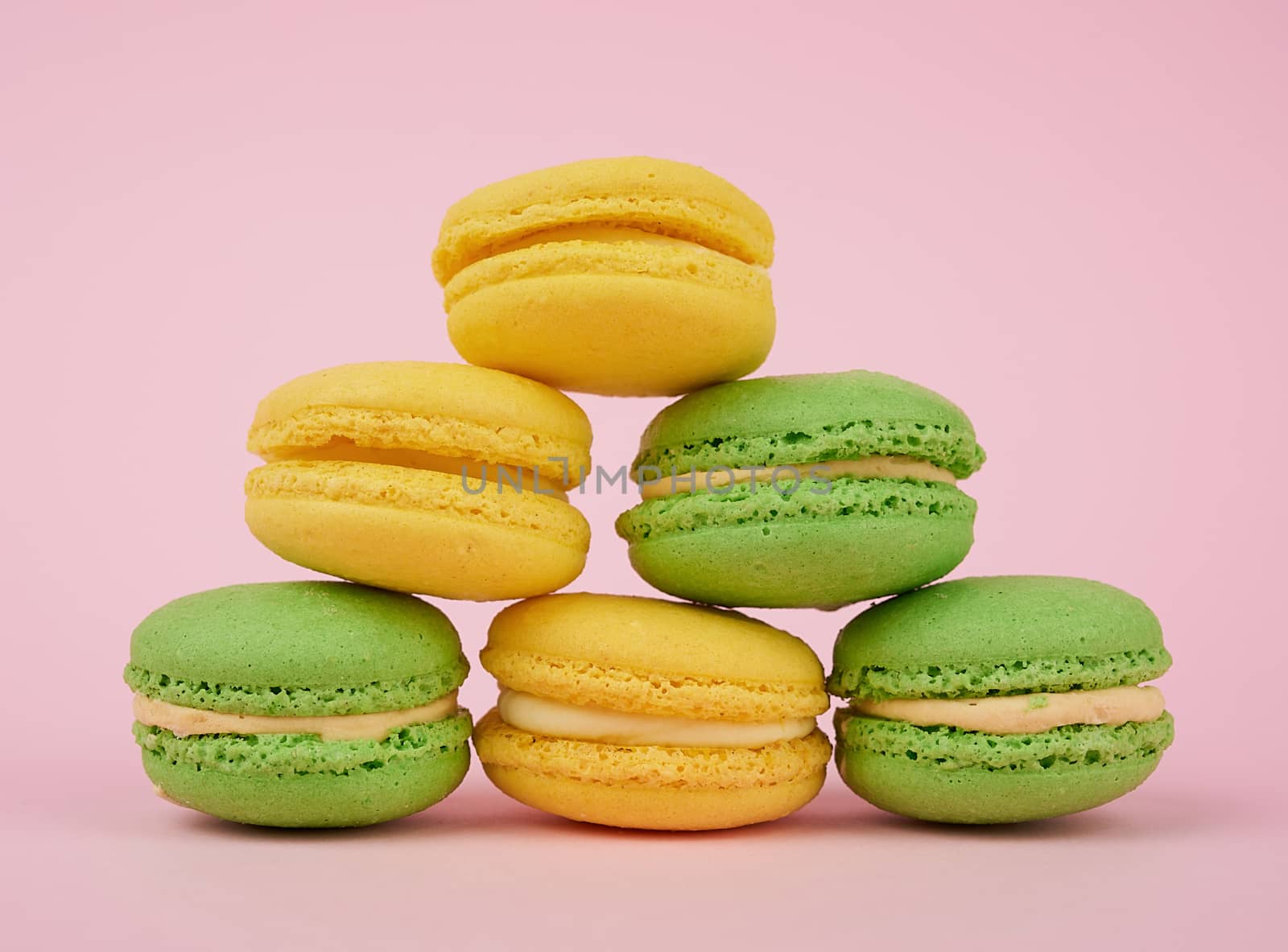 stack of yellow and green round almond flour cakes macarons with cream on a pink background, delicious cake