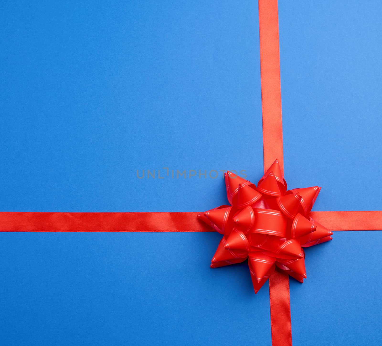 red silk ribbon crossed on a  blue background in the middle of a red bow, imitation of tying a gift, top view