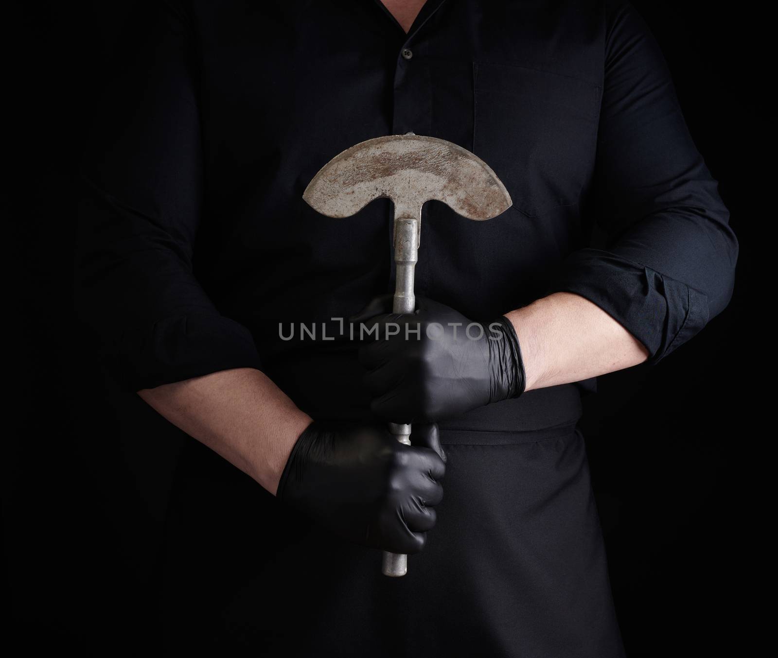 man in black clothes, latex gloves holds a vintage metal ax-knife for meat and vegetables, dark background