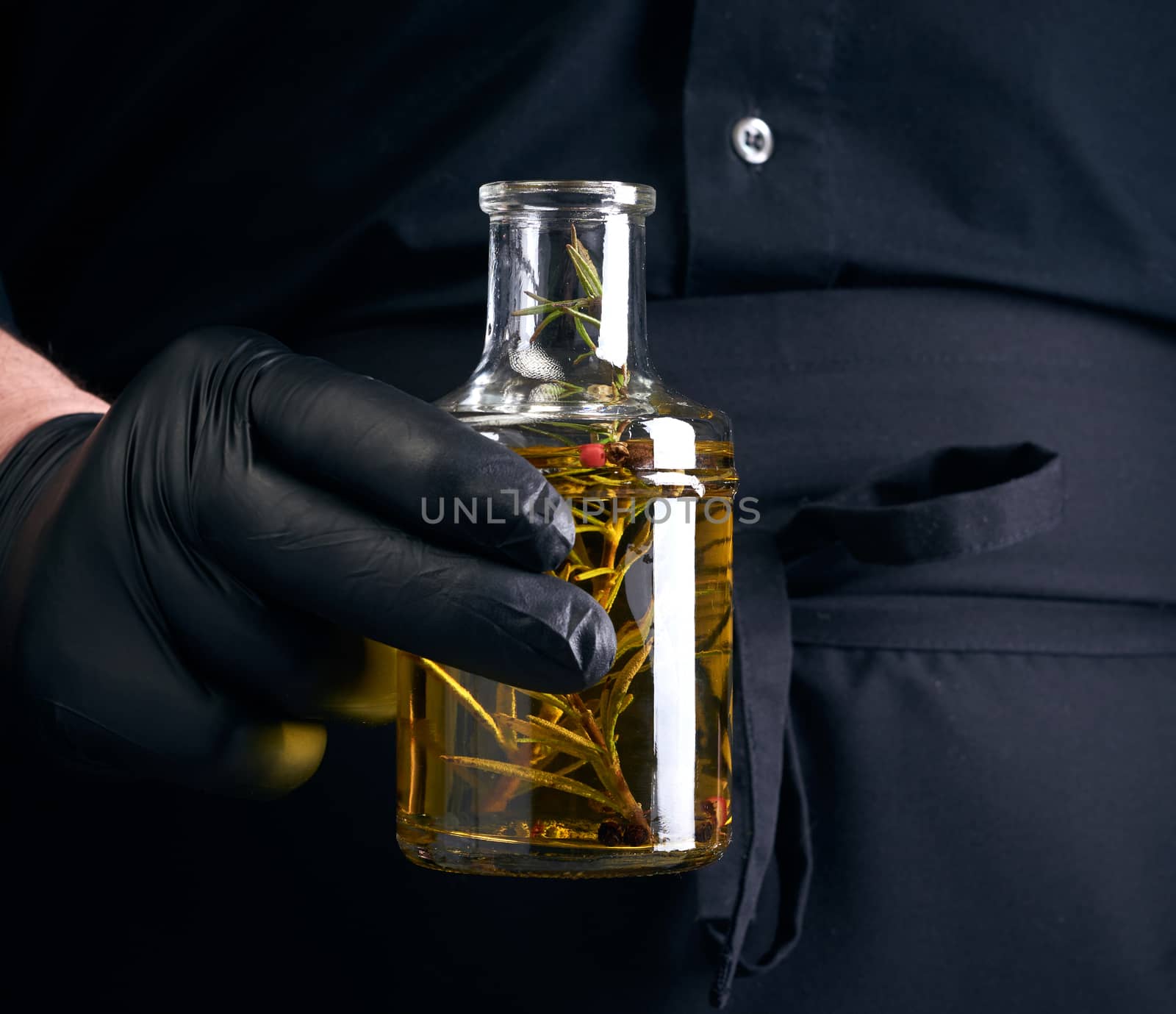 man in black clothes, latex gloves holds a transparent bottle with olive oil, low key, close up