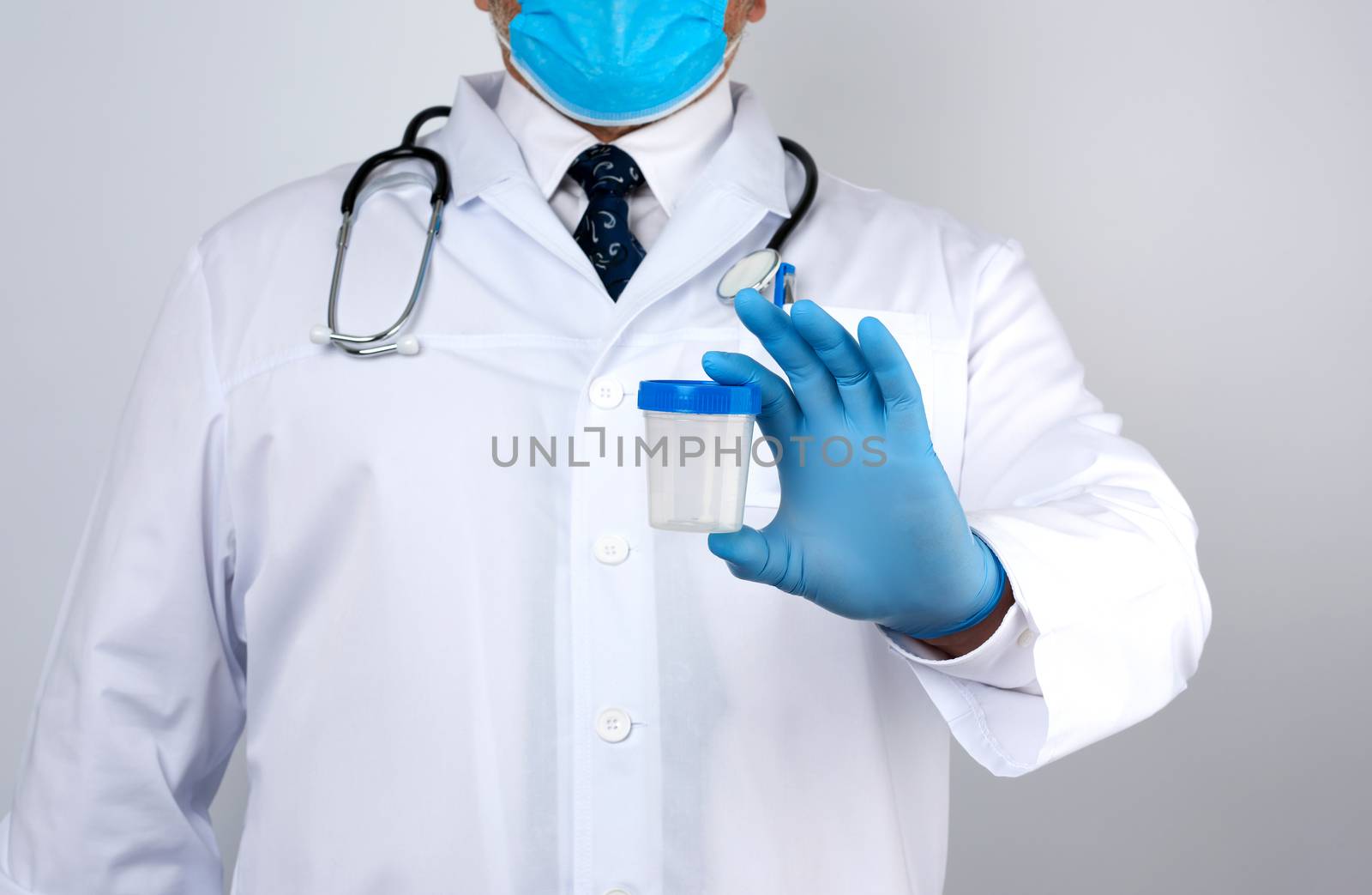 male doctor in a white coat and tie stands and holds a empty plastic container for urine specimen, wearing blue sterile medical gloves