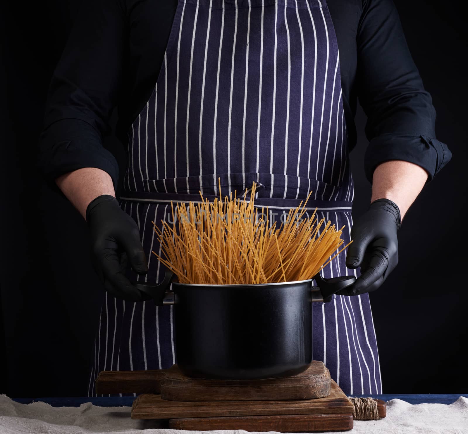 uncooked yellow long spaghetti in a black metal pan and a chef in a striped apron, cooking process