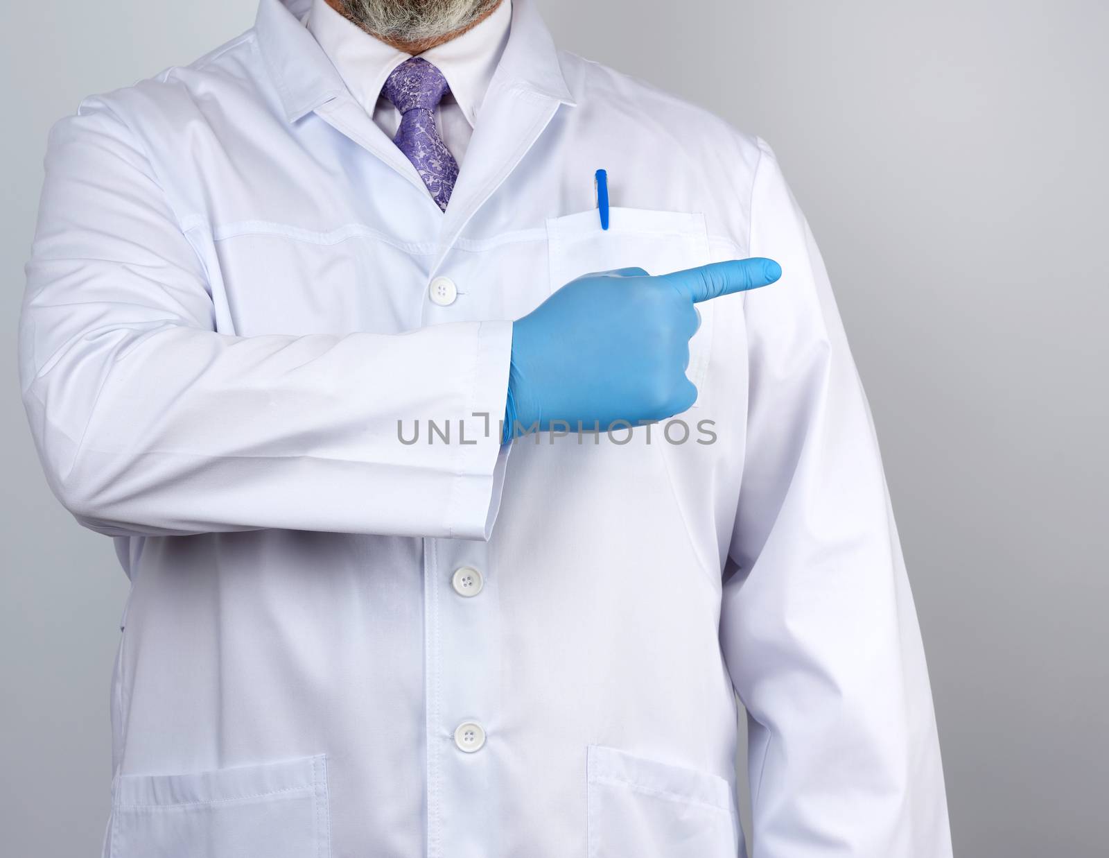 medic man in white coat with buttons, on hands wearing blue sterile gloves, showing hand gesture indicating the subject, white background