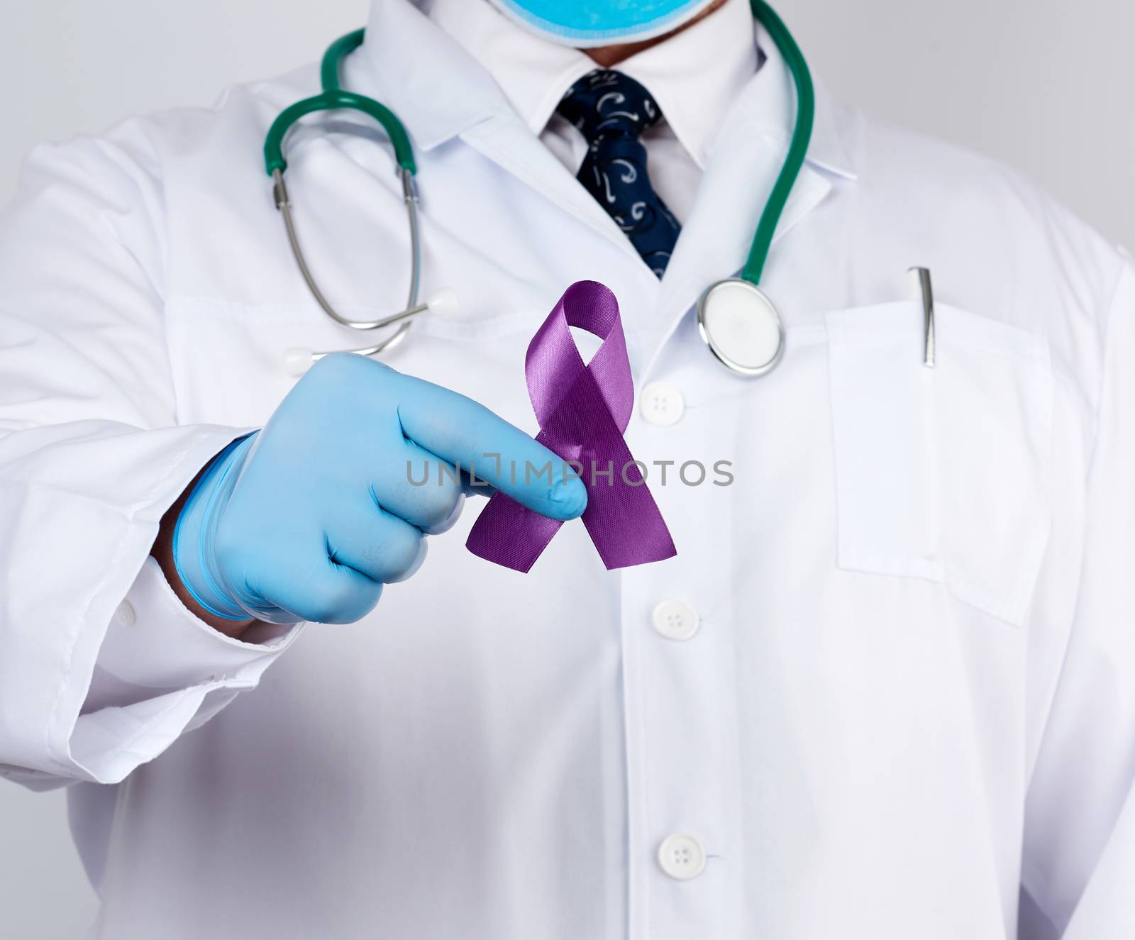 male doctor in a white coat and tie stands and holds a purple silk ribbon in the form of a loop, wearing blue sterile medical gloves. Symbol of early research and disease control, Alzheimer's disease