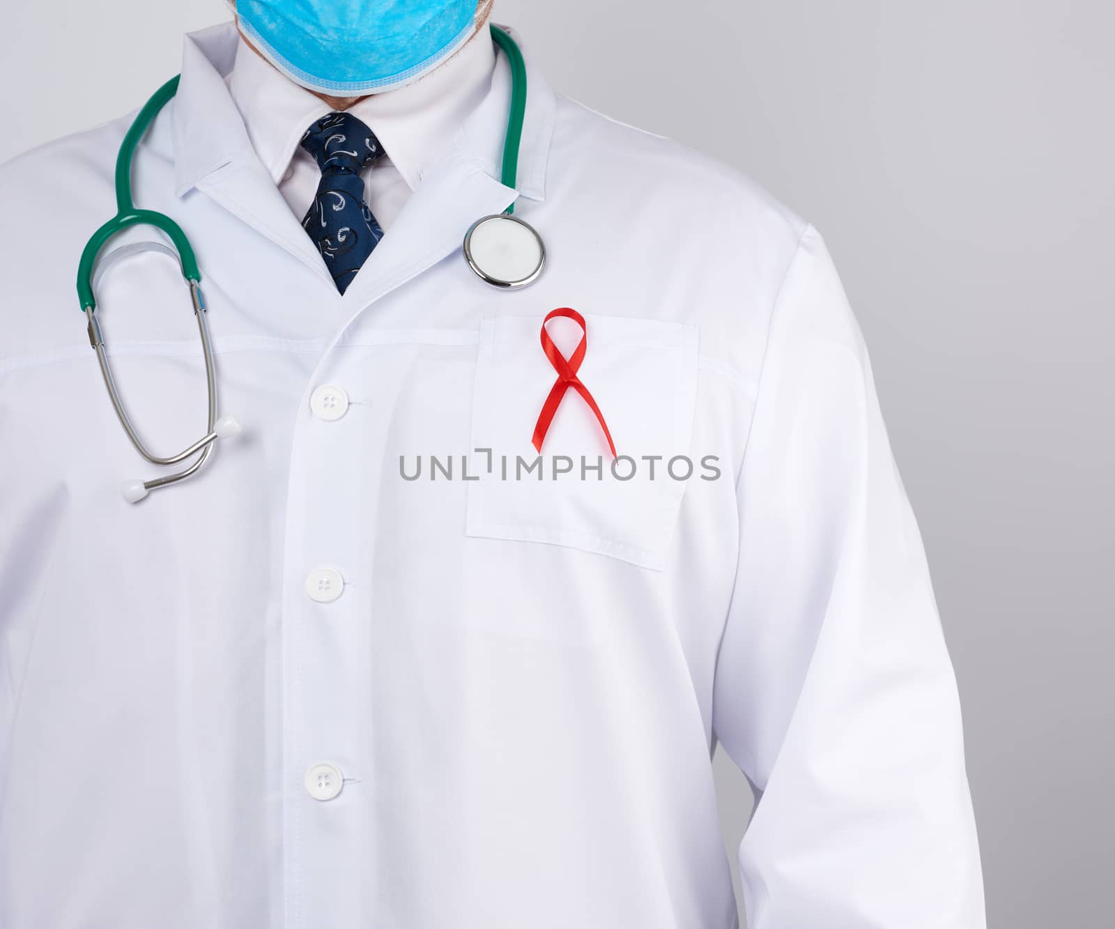 doctor in a white coat and tie is standing on a white background, red silk ribbon is hanging on his chest, symbol of the fight against disease AID