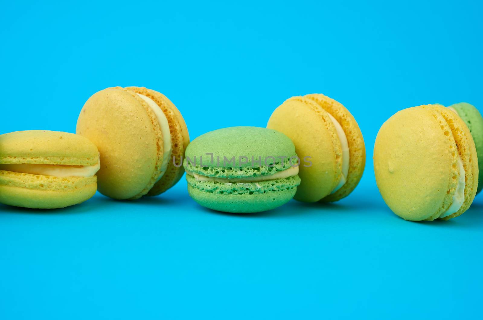multi-colored round baked macarons cakes on a light blue background, dessert stands in a row, close up