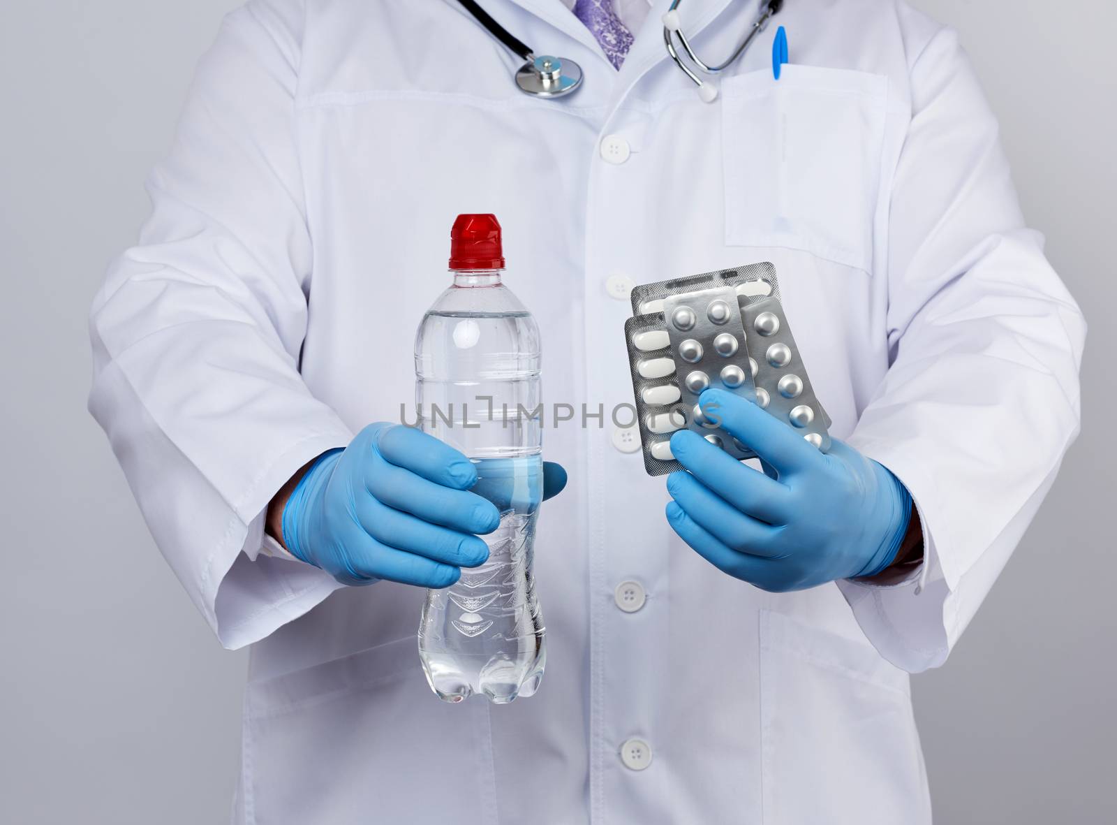 adult doctor therapist is dressed in a white uniform coat and blue sterile gloves is standing and holding a stack of pills in blister packs, white background