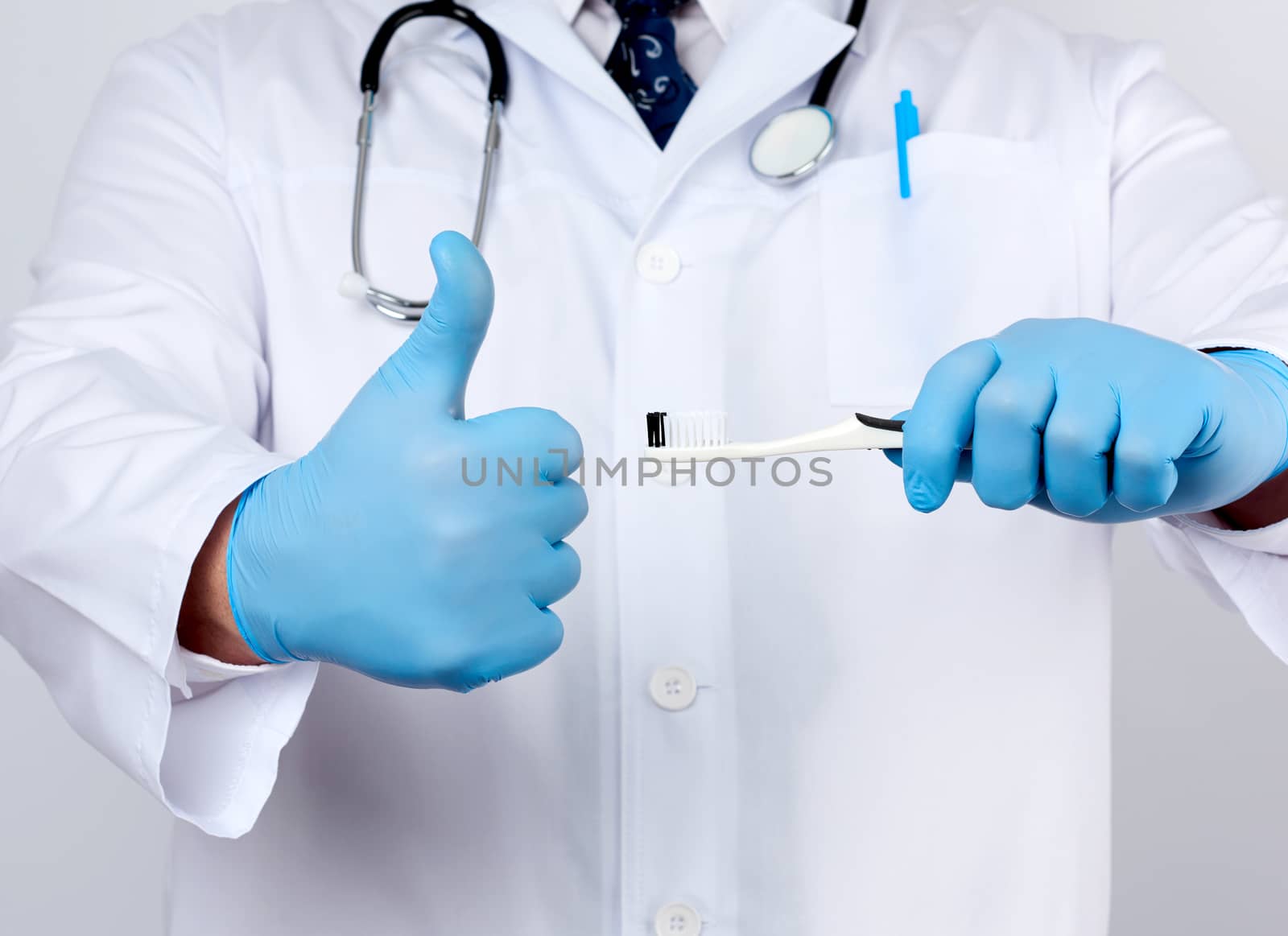 adult doctor therapist is dressed in a white robe uniform and blue sterile gloves is standing and holding a toothbrush, daily brushing concept, white background