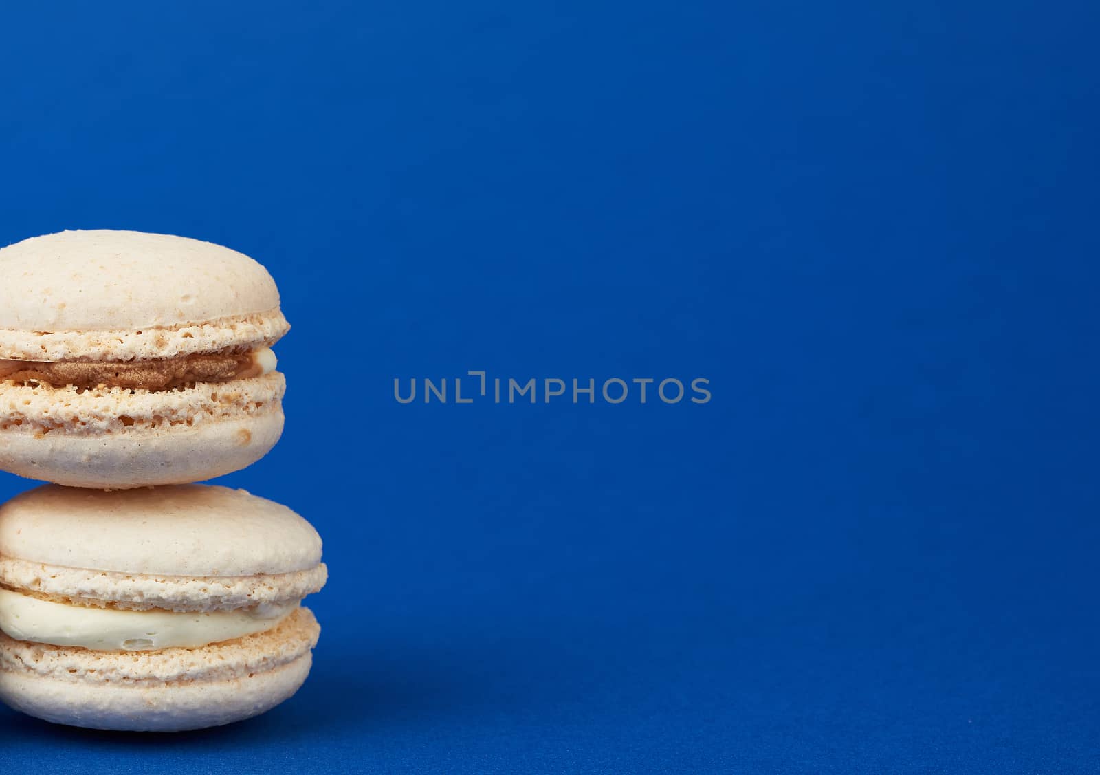 stack of white round baked almond flour cakes macarons on a dark blue background, delicious popular french dessert, copy space