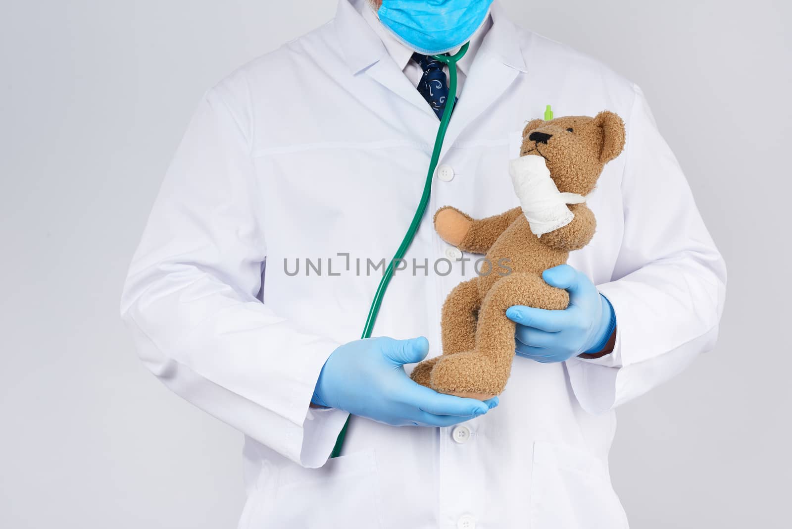 pediatrician in a white coat, blue latex gloves holds a brown teddy bear with a bandaged paw, toy treatment