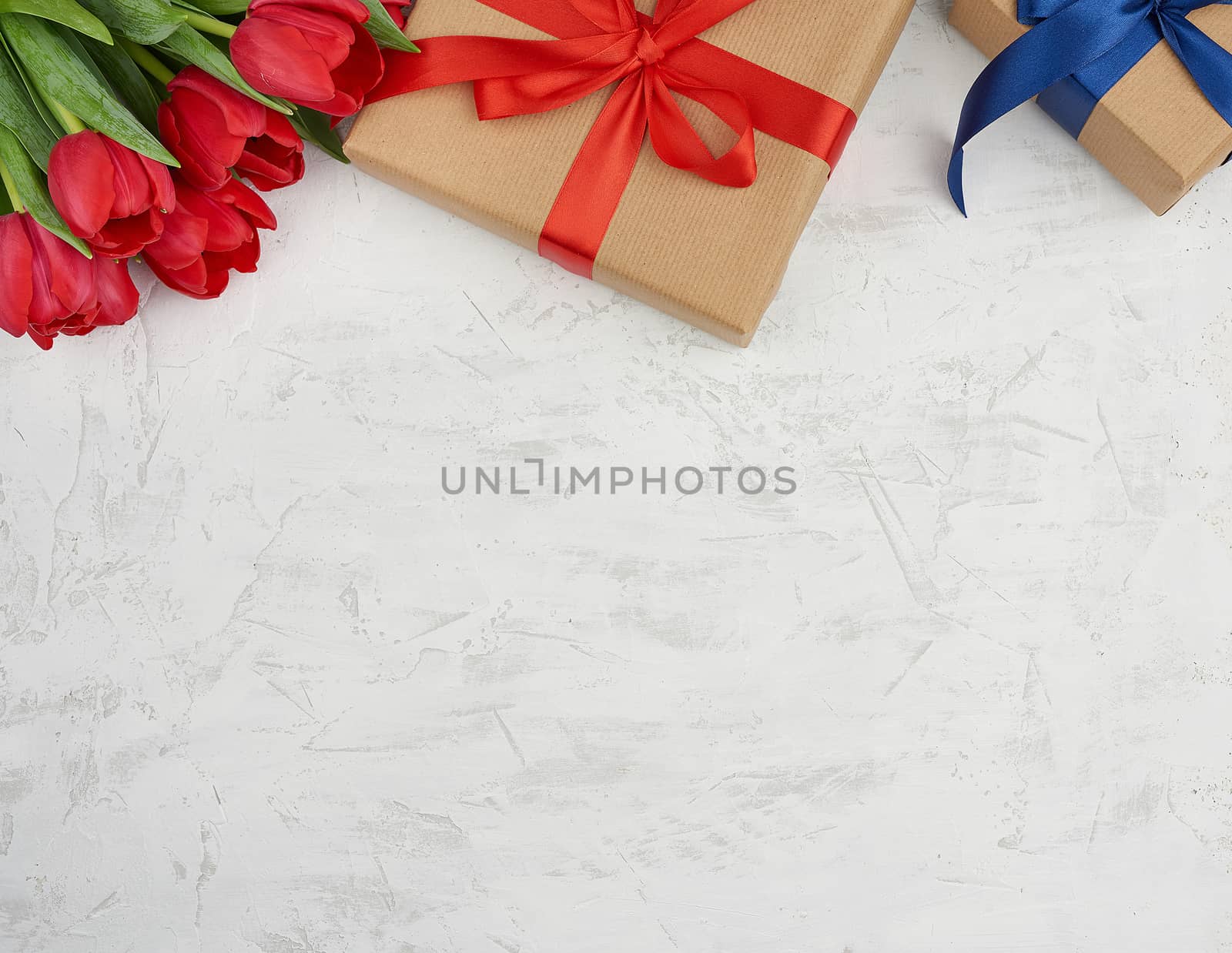 bouquet of red blooming tulips with green leaves, wrapped gifts in brown craft paper and tied with silk ribbon on a white background. Festive backdrop for birthday, Valentine's day, anniversary