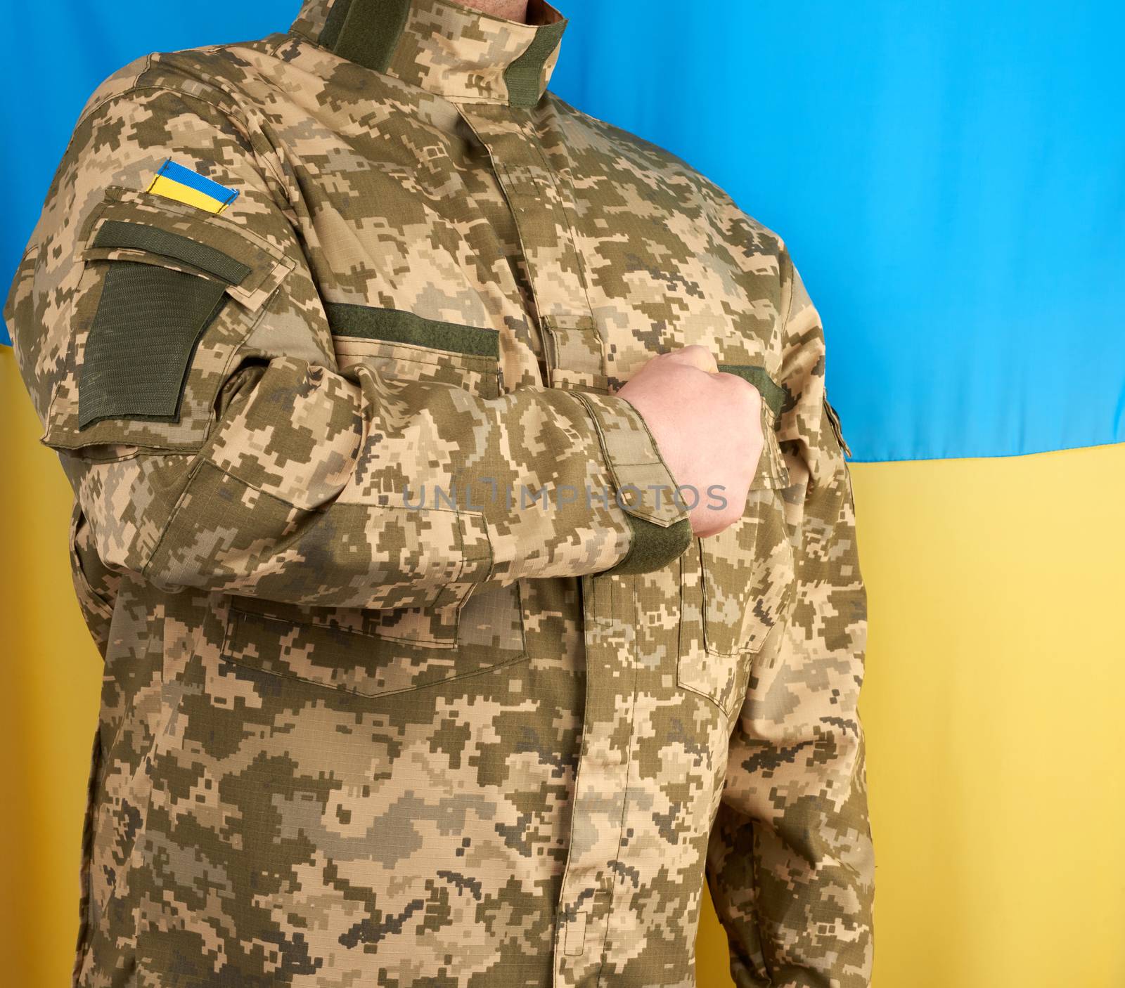Ukrainian man a warrior dressed in a military pixel uniform stands against the background of the national flag of Ukraine, soldier put his right hand to his chest as a sign of respect, honor