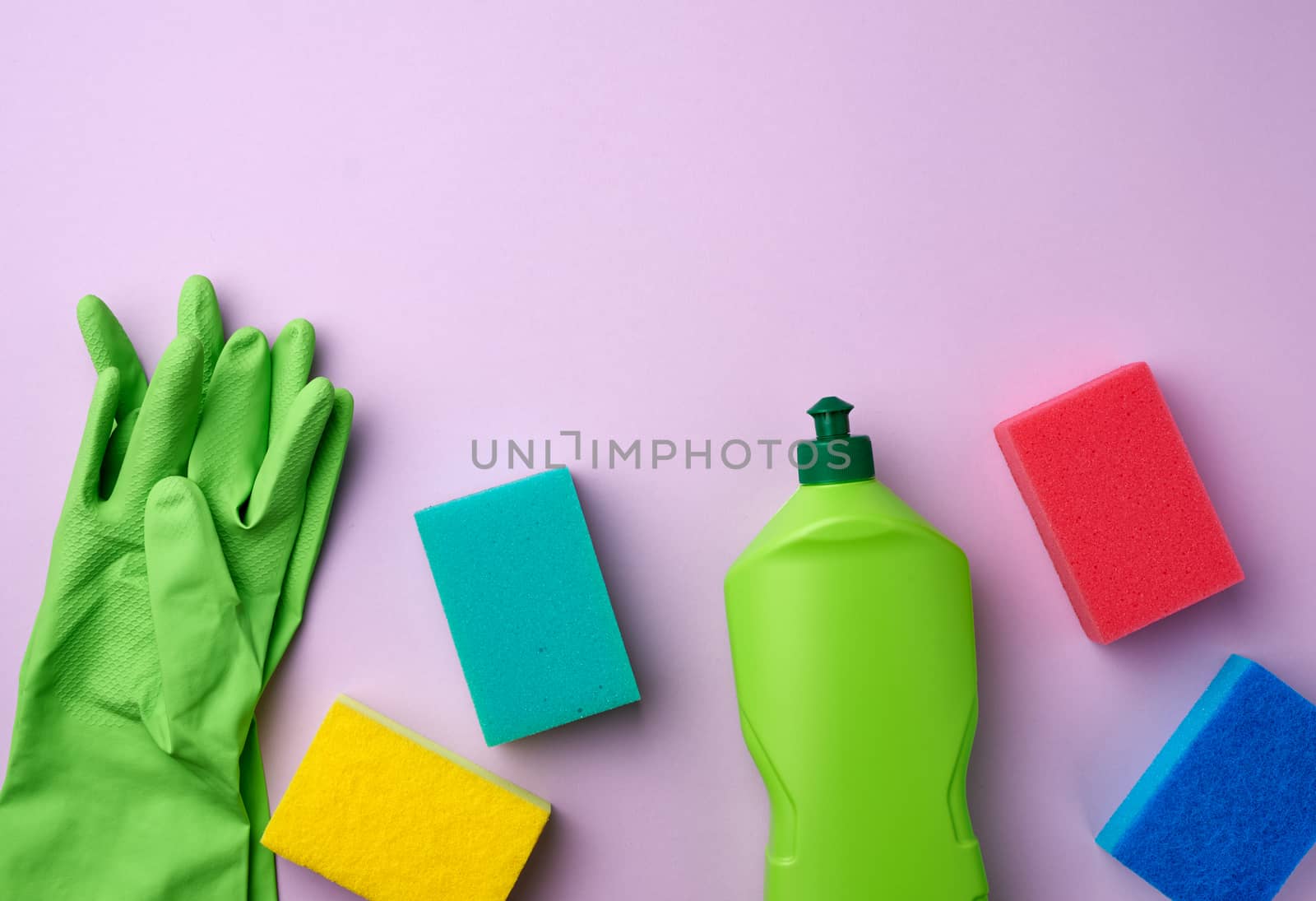 purple rubber gloves for cleaning, multi-colored sponges, cleaning fluid in a green plastic bottle on a purple background, place for text, flat lay